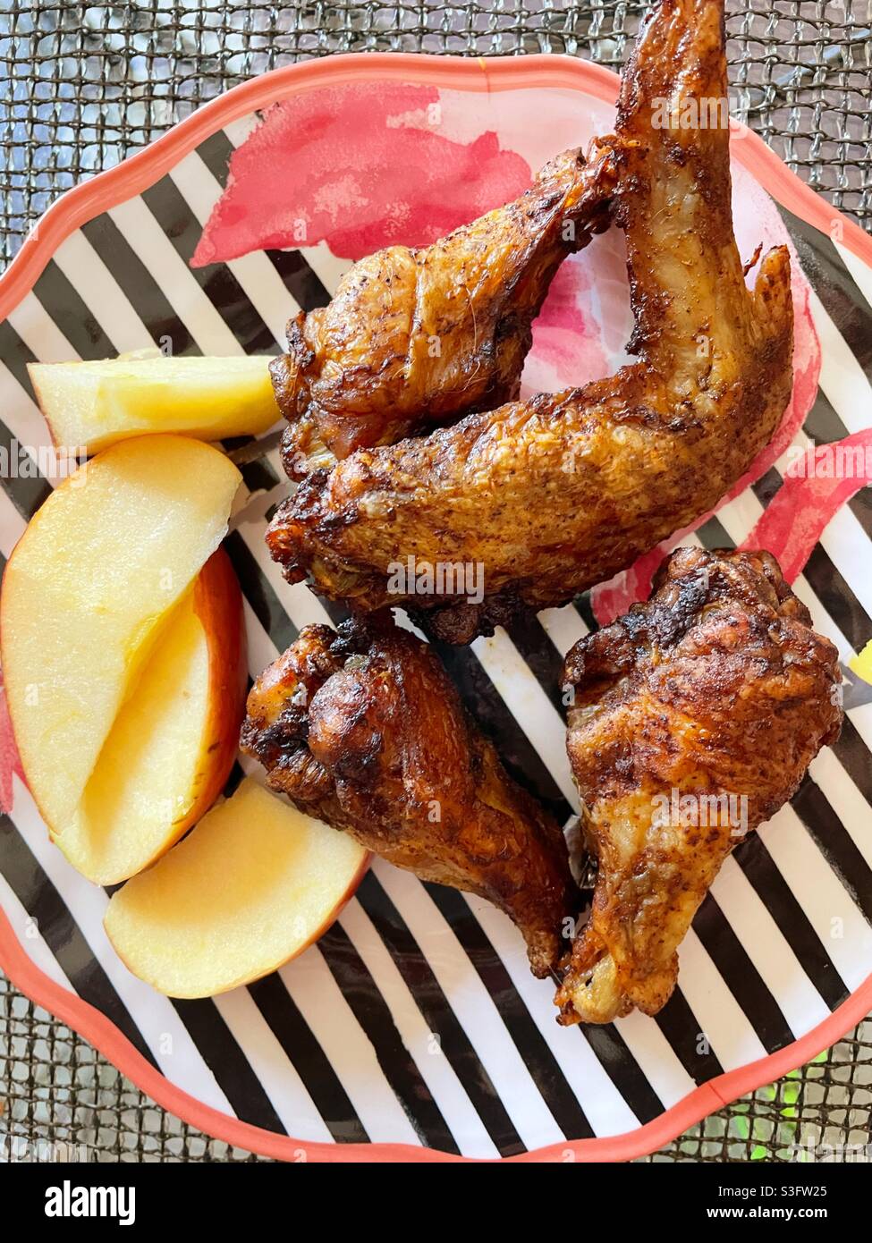 Un déjeuner de fête composé d'ailes de poulet et de tranches de pomme fraîche sur une assiette de kitsch rose flamant à rayures, USA - Image de stock capturée avec un smartphone