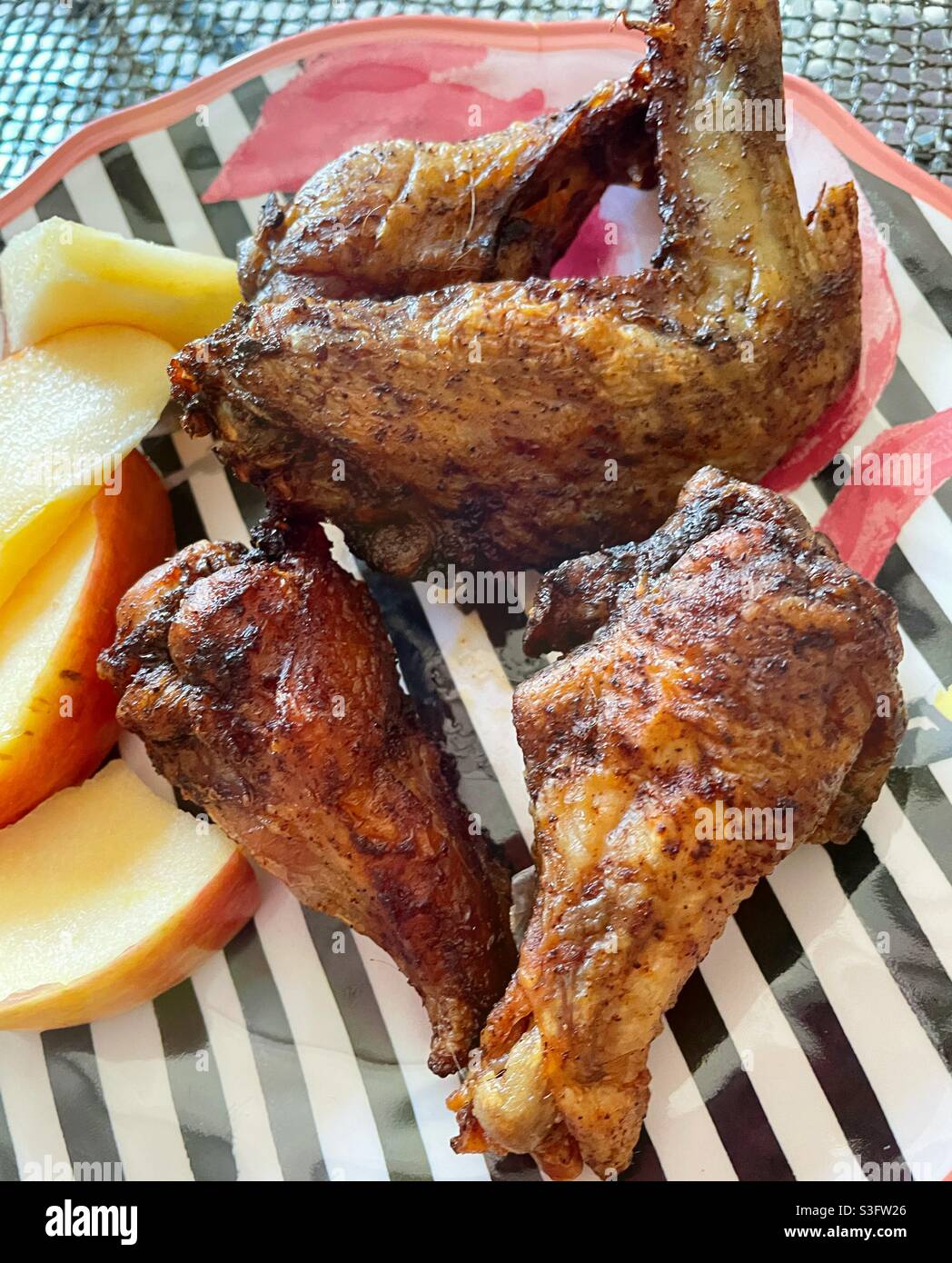Un déjeuner fantaisiste d'ailes de poulet rôtisserie et de tranches de pomme sur une plaque de mangoute noire et blanche à rayures flammantes, USA - Image de stock capturée avec un smartphone
