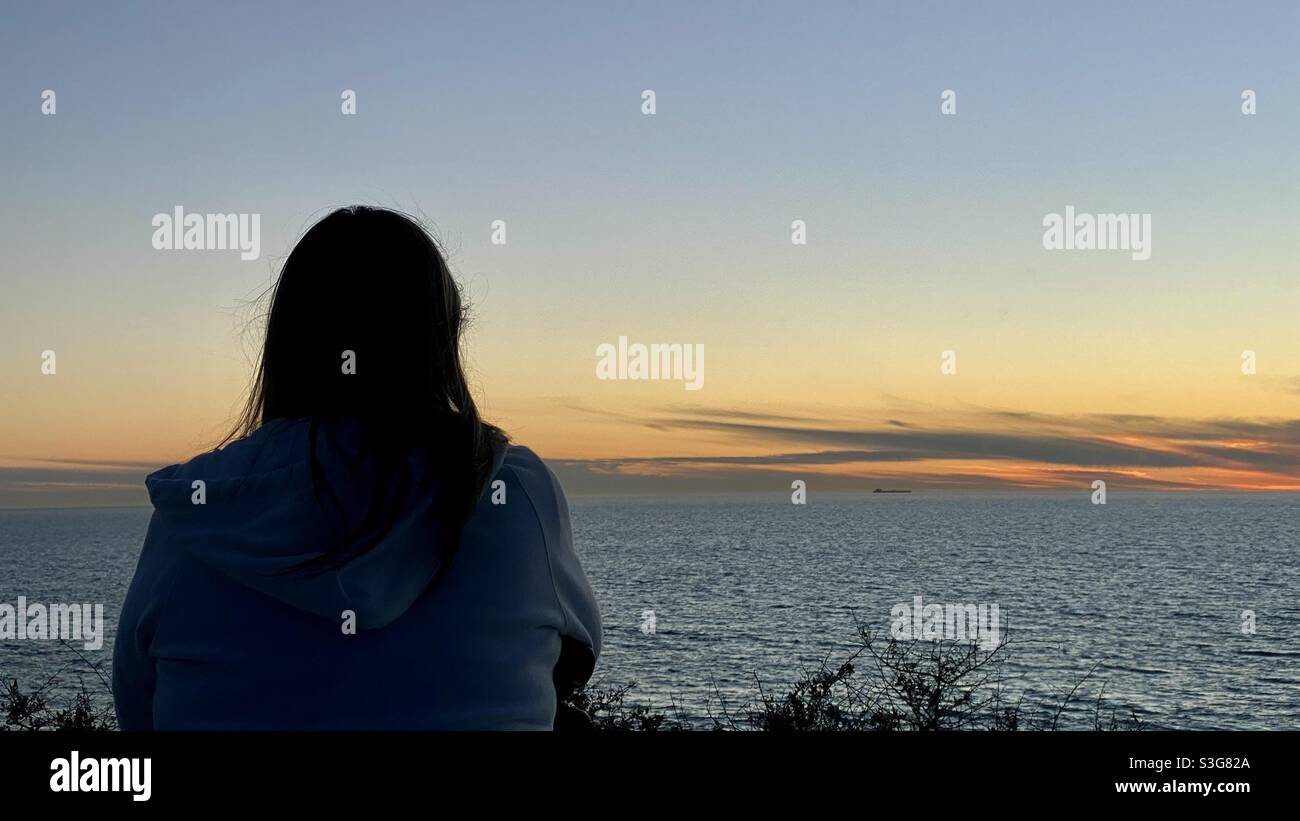 Vue de derrière, femme silhouetée qui a vue sur l'océan Pacifique au crépuscule Banque D'Images