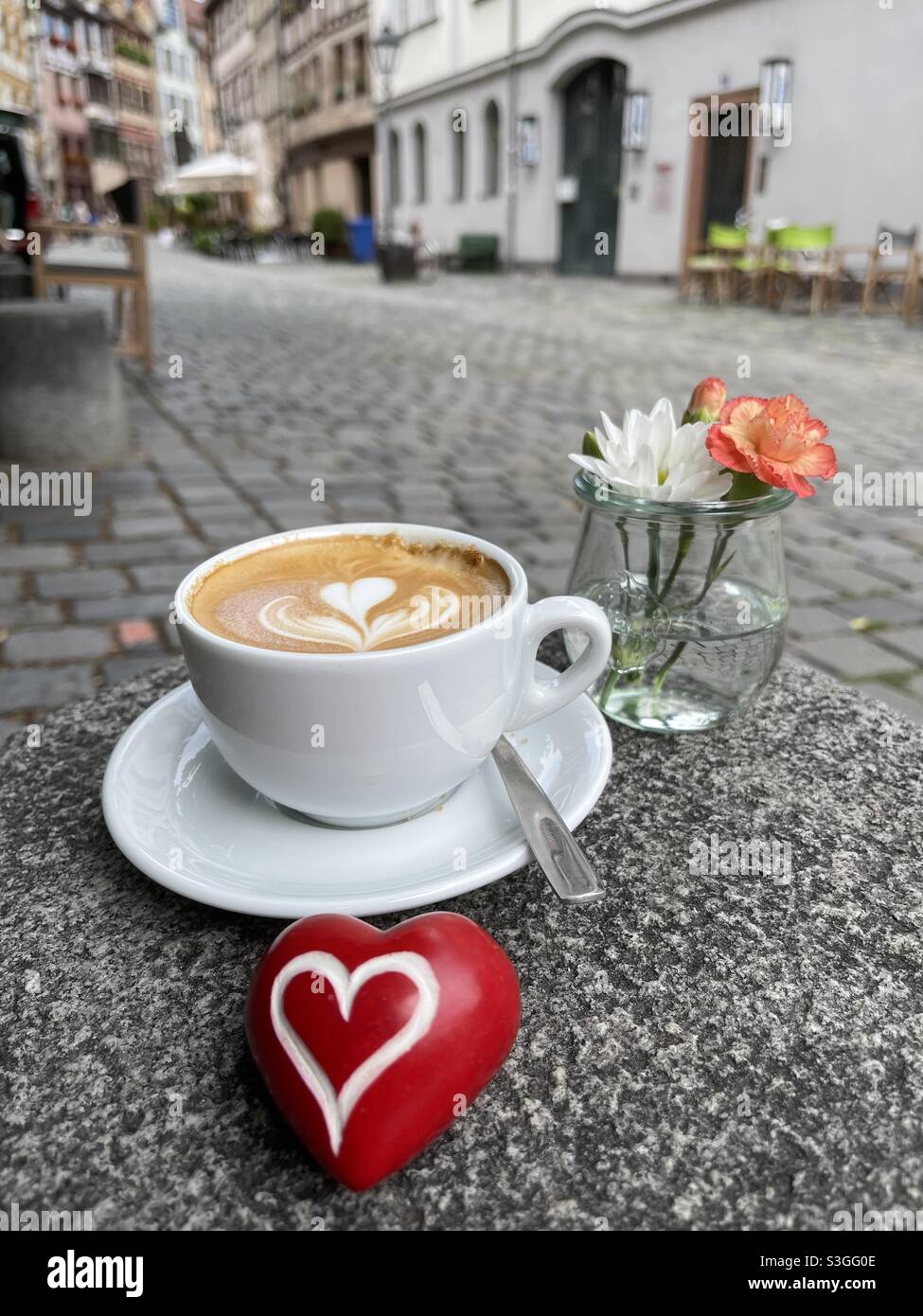 Un agréable moment de détente au bar avec un cappuccino chaud, des fleurs et un coeur en pierre rouge Banque D'Images