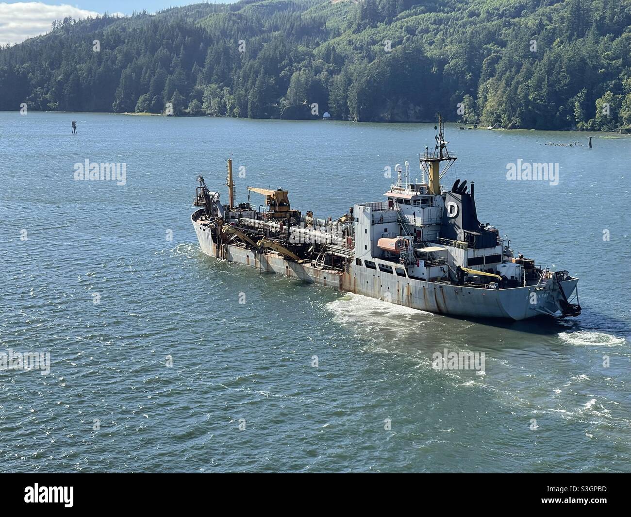 Bateau-dragueur sur le fleuve Columbia, naviguant du port de Portland, aux États-Unis, jusqu'à l'océan Pacifique. En arrière-plan est dense forêt de conifères. Banque D'Images