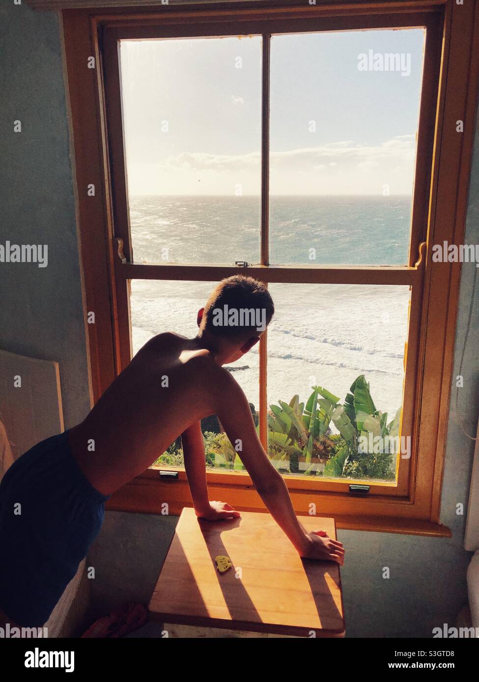 Un jeune garçon qui regarde par la fenêtre au soleil se lève sur l'océan Indien Banque D'Images