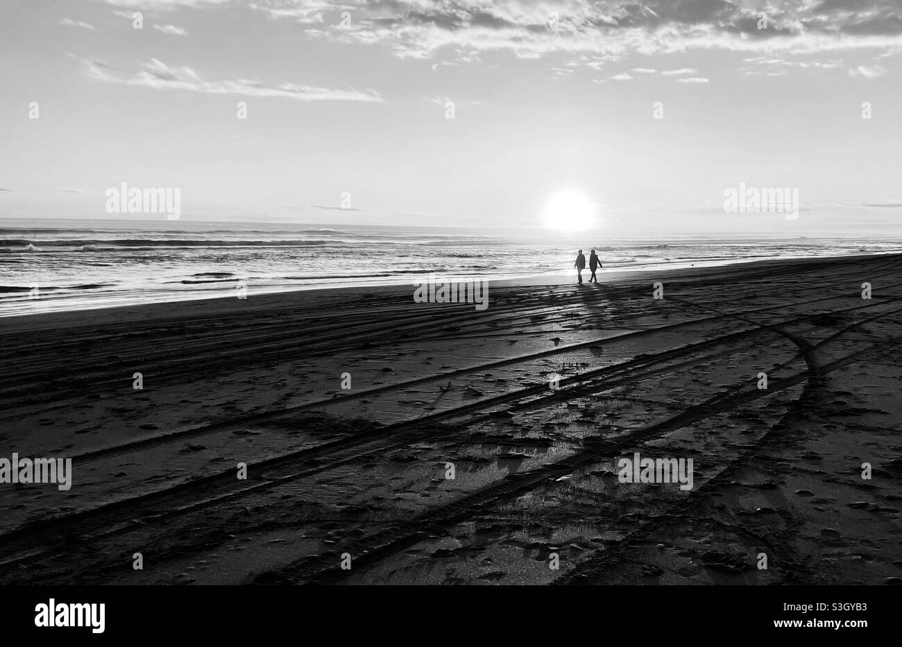 Plage de Castlecliff, Whanganui, Nouvelle-Zélande: Deux personnes marchent le long de la plage au coucher du soleil Banque D'Images