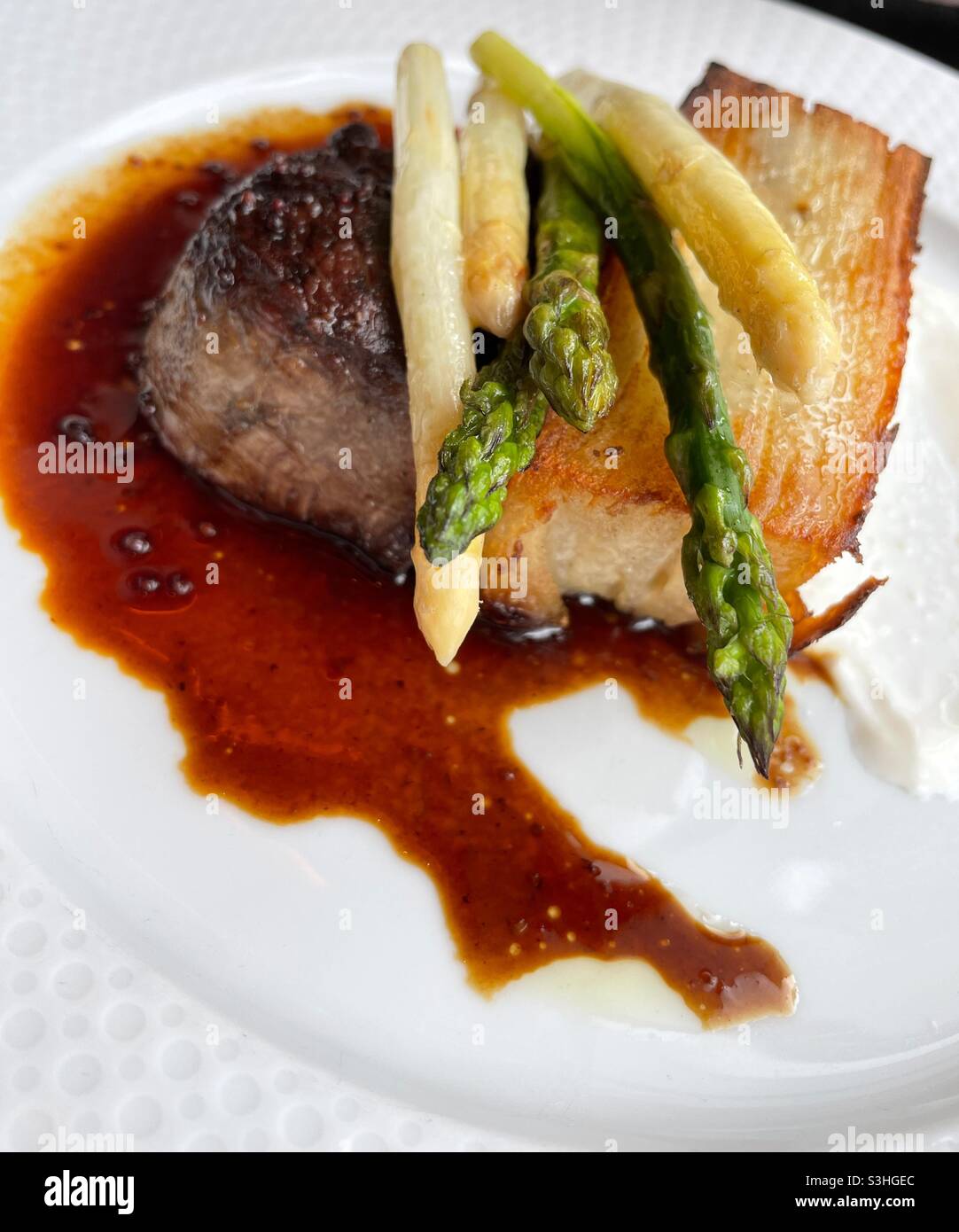 Gros plan sur un plat principal composé d'un petit filet mignon aux asperges glacées et à la sauce crème fraiche dans un restaurant haut de gamme, New York, États-Unis - Image de stock capturée avec un smartphone