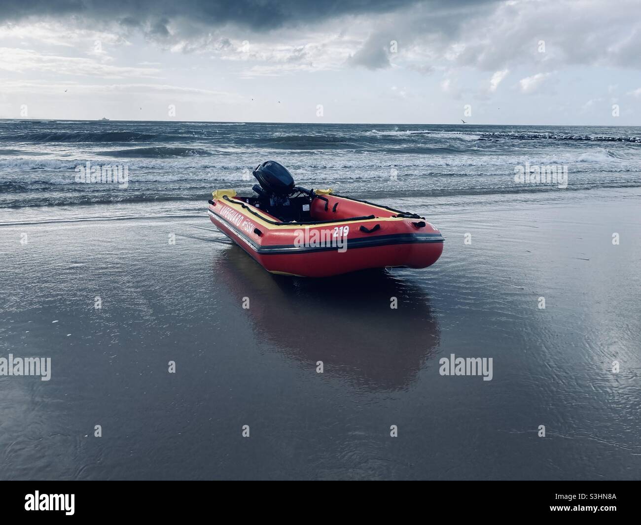 un bateau gonflable motorisé se trouve dans l'eau peu profonde de la plage et des nuages sombres peuvent être vus dans le ciel Banque D'Images