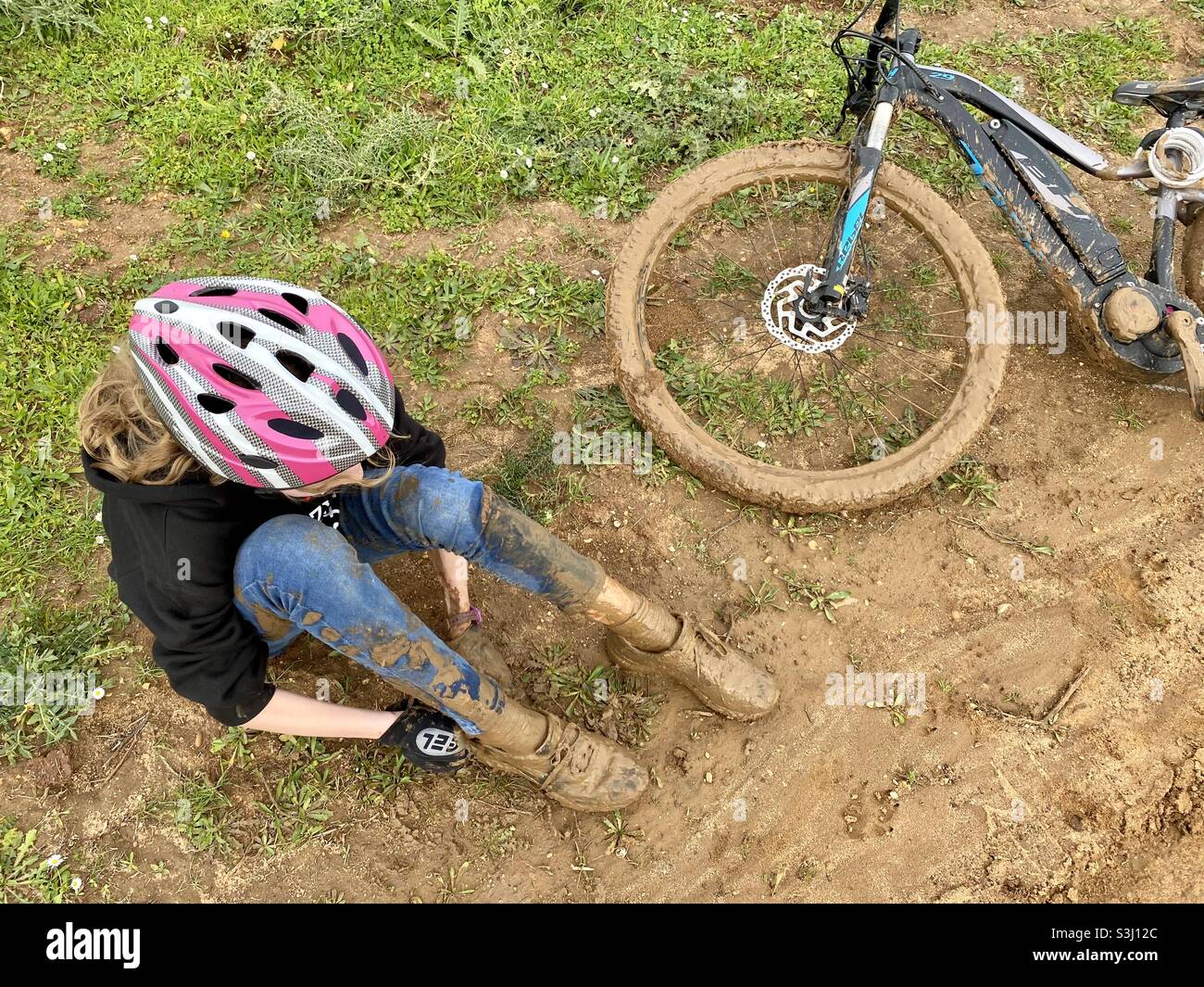 Vue en grand angle d'une fille couverte de boue et assise sur le sol à côté de son vélo de montagne boueux Banque D'Images