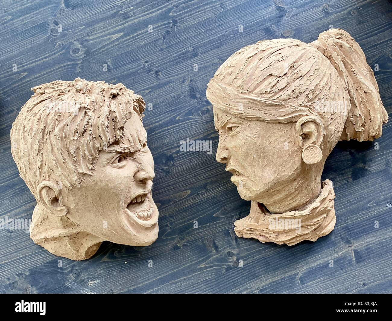 Sculpture en argile de deux visages interagissant avec un fond en bois - Image de stock capturée avec un smartphone