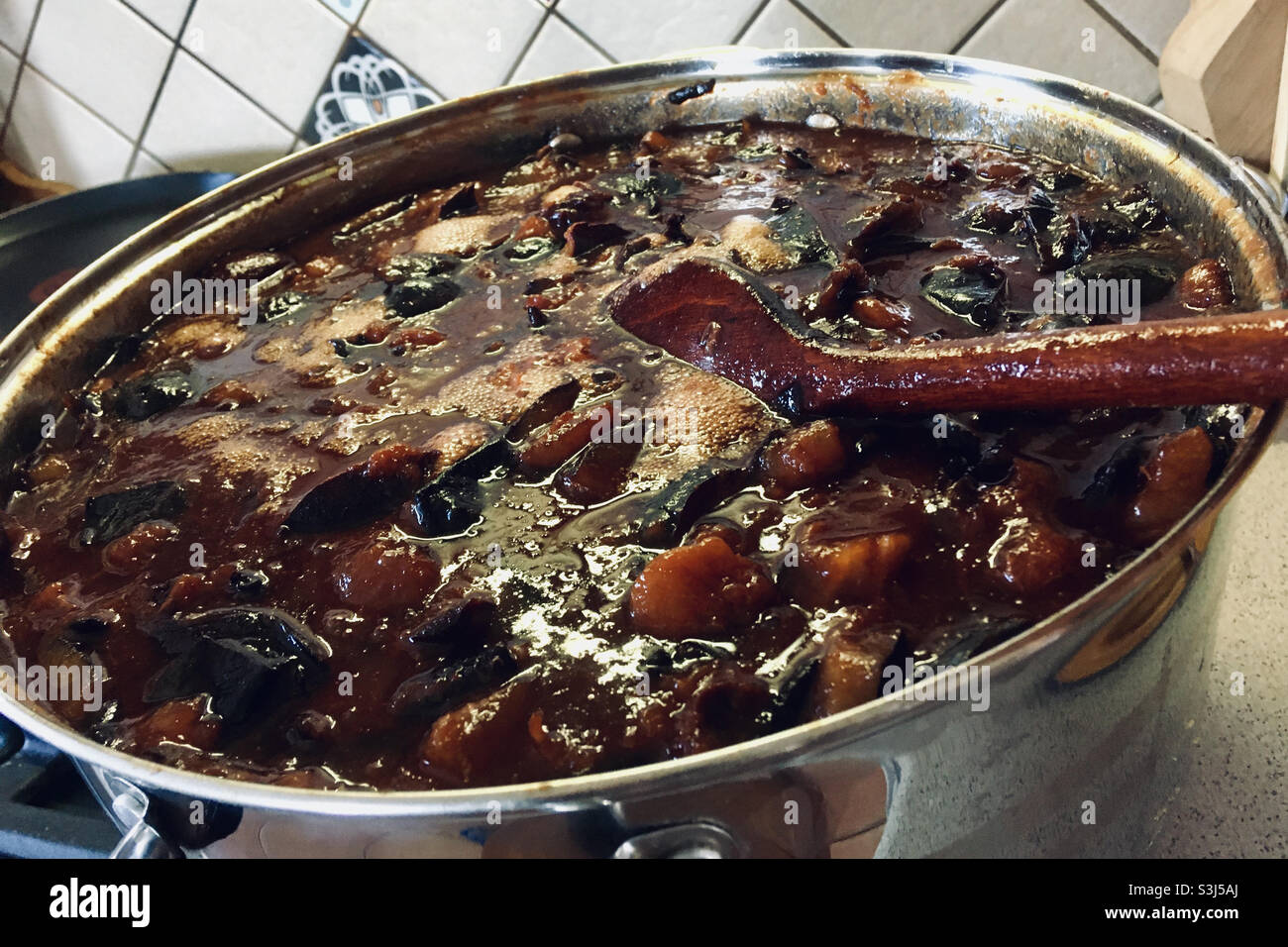 Faire de la confiture de prunes sans sucre ni conservateur. Cuillère en bois de confiture de prune bouillante dans la cuisine. - Image de stock capturée avec un smartphone
