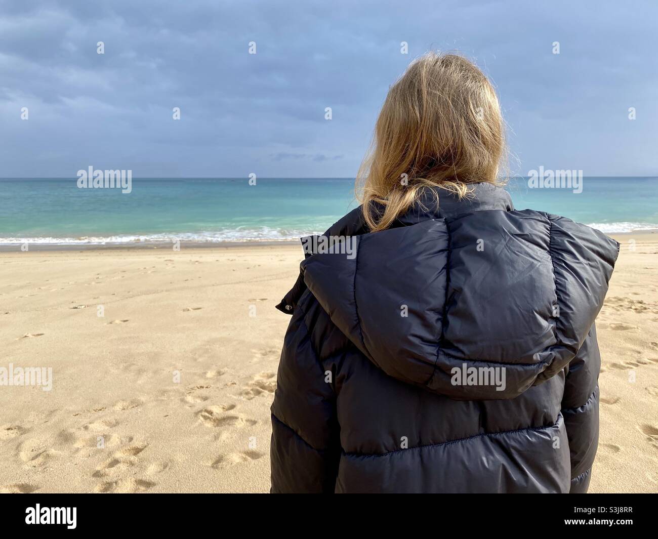 Fille portant un manteau d'hiver et se tenant sur une plage de sable qui  donne sur la mer Photo Stock - Alamy