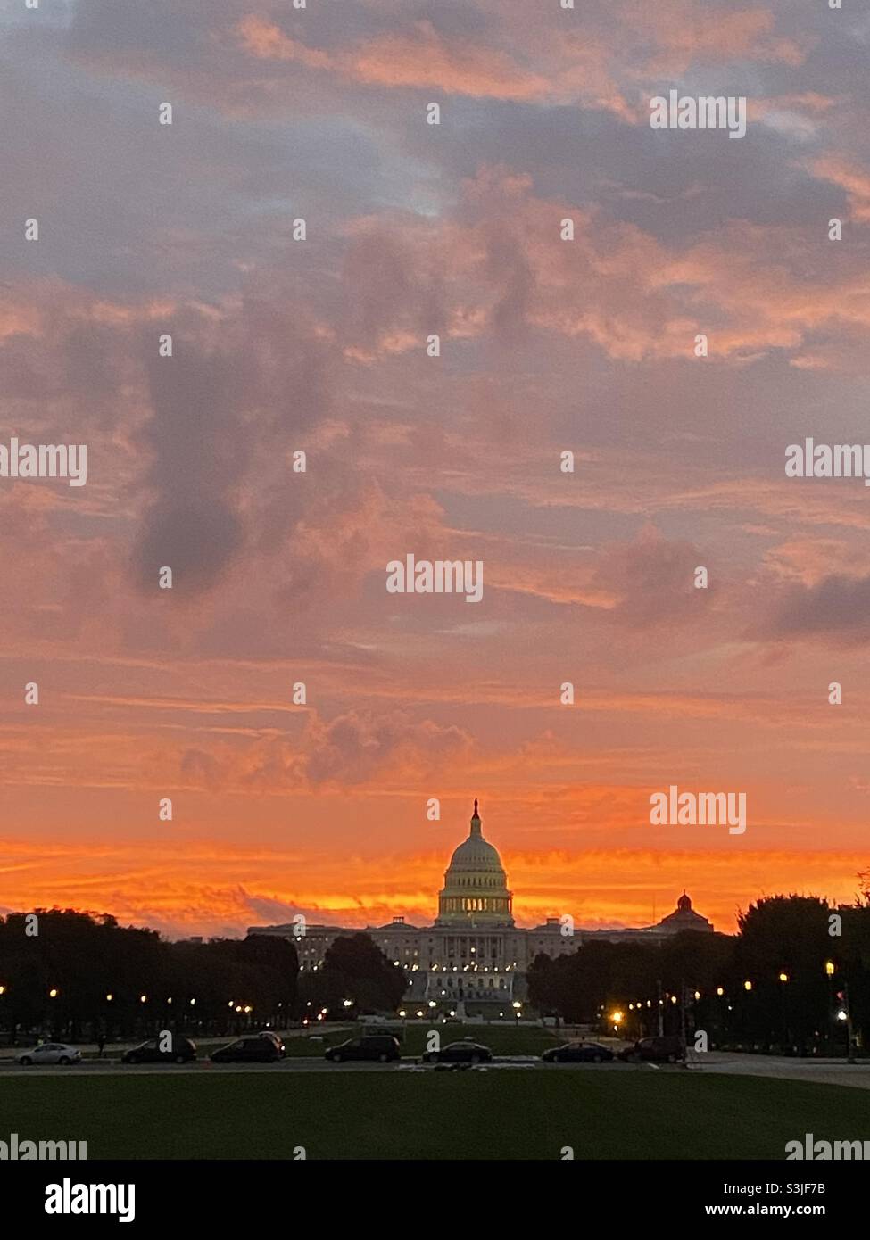 Le ciel est éclairé dans des tons de rose, d'orange et d'or tandis que le soleil se lève derrière le bâtiment du Capitole des États-Unis à Washington, D.C. - Image de stock capturée avec un smartphone