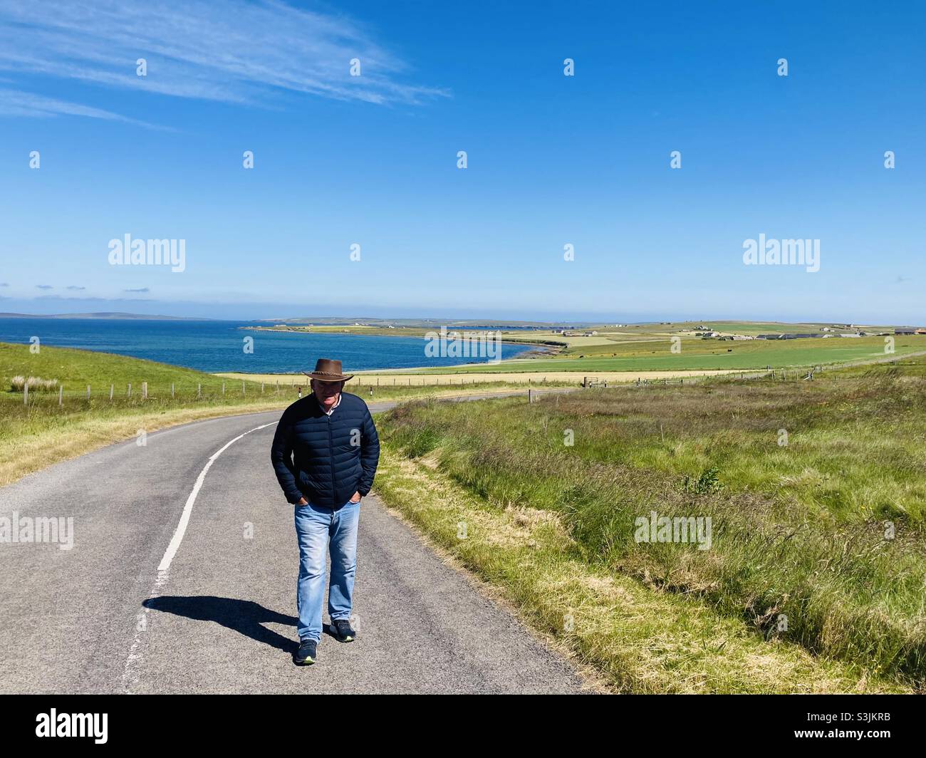 Homme marchant sur une route sur Flotta, Orkney.Île de la Flotta en arrière-plan et flux de scaca.Écosse Banque D'Images