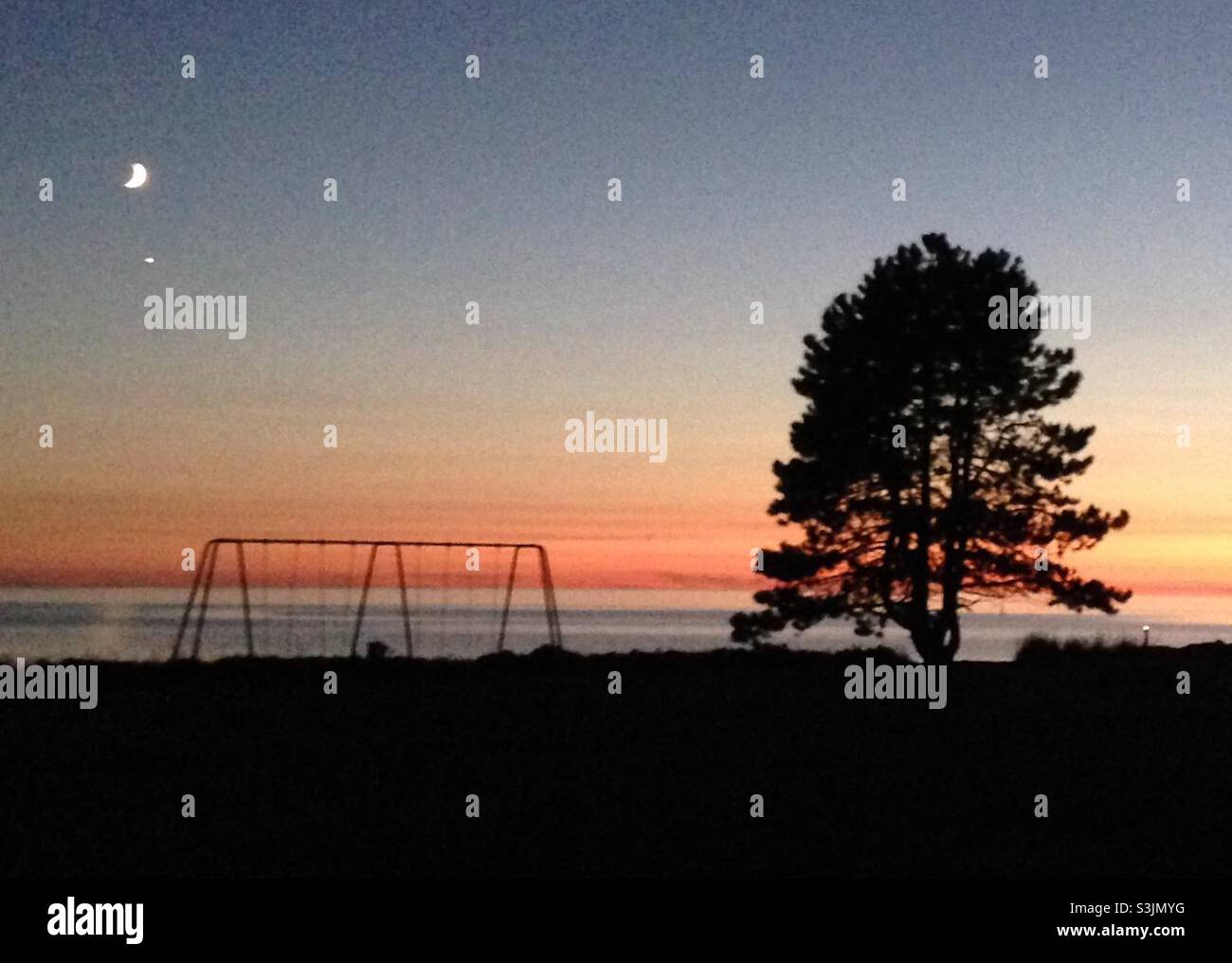 Petit parc près du bord de l'eau au coucher du soleil avec la lune et Vénus Banque D'Images