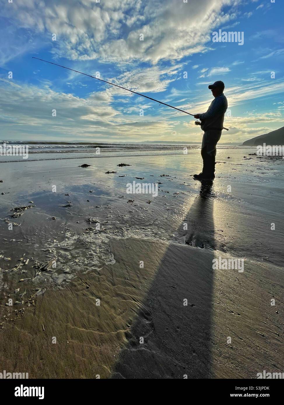 Silhoueté pêcheur à la ligne sur une plage gallois au coucher du soleil Banque D'Images