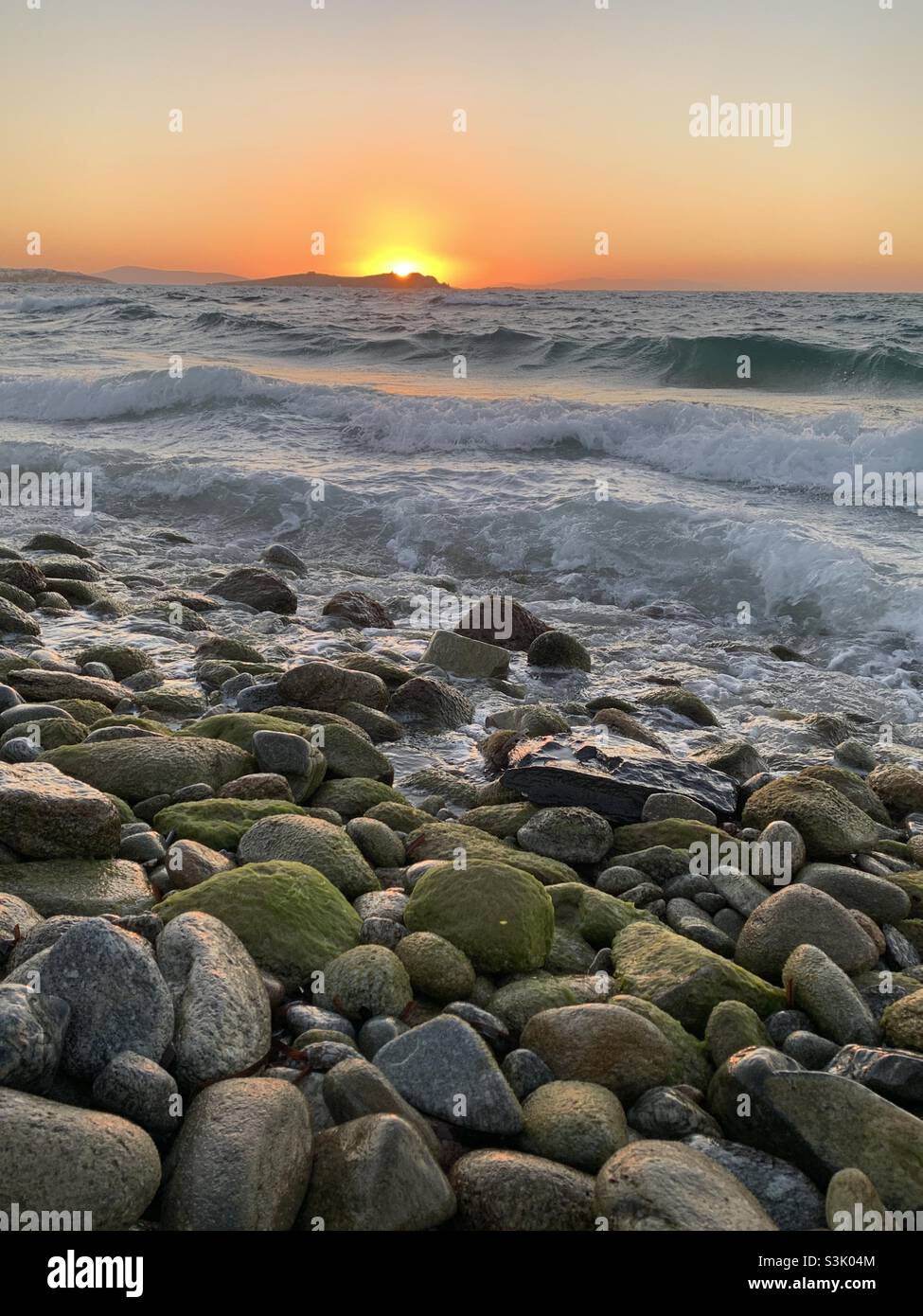 Coucher de soleil sur des pierres vertes lisses à la plage en Grèce Banque D'Images