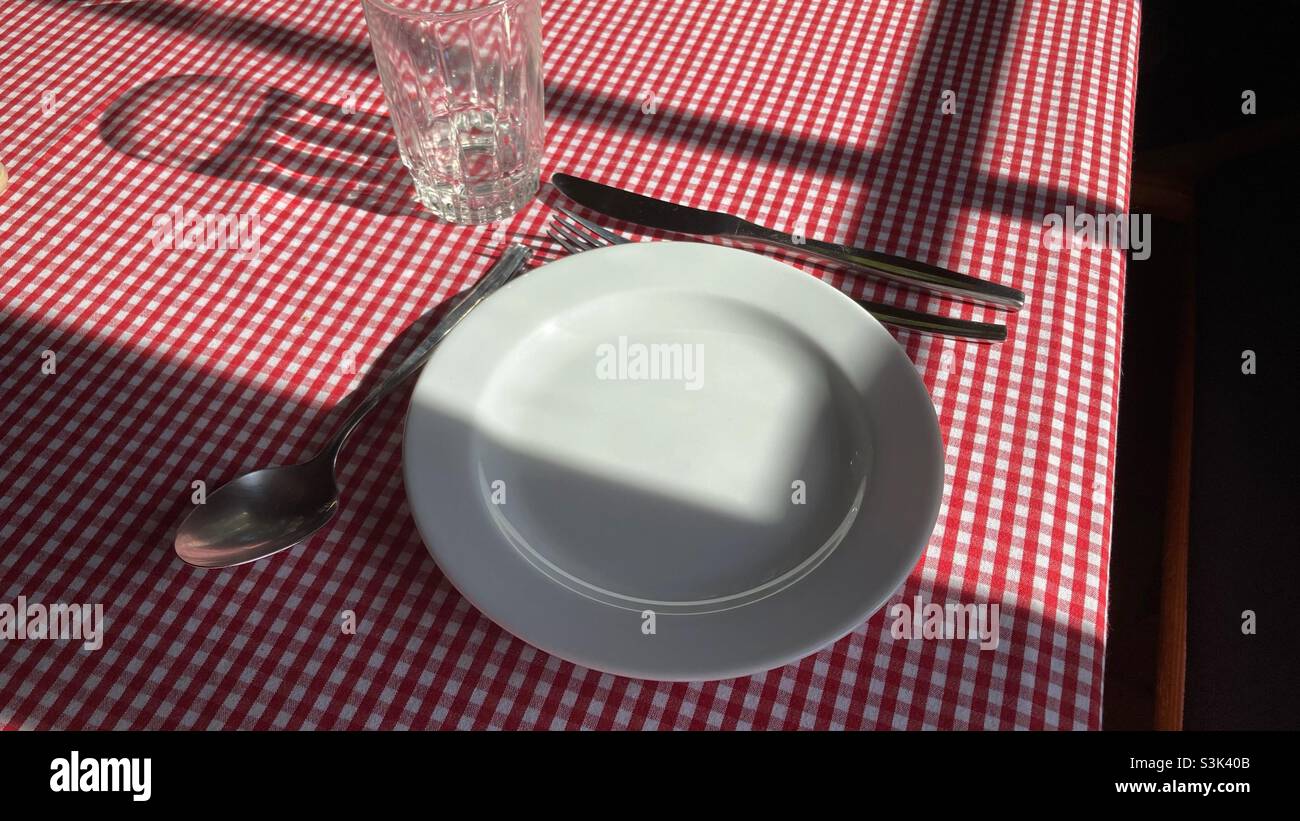 Vider la plaque et un verre, une fourchette et un couteau sur une table avec un chiffon de table à carreaux Banque D'Images