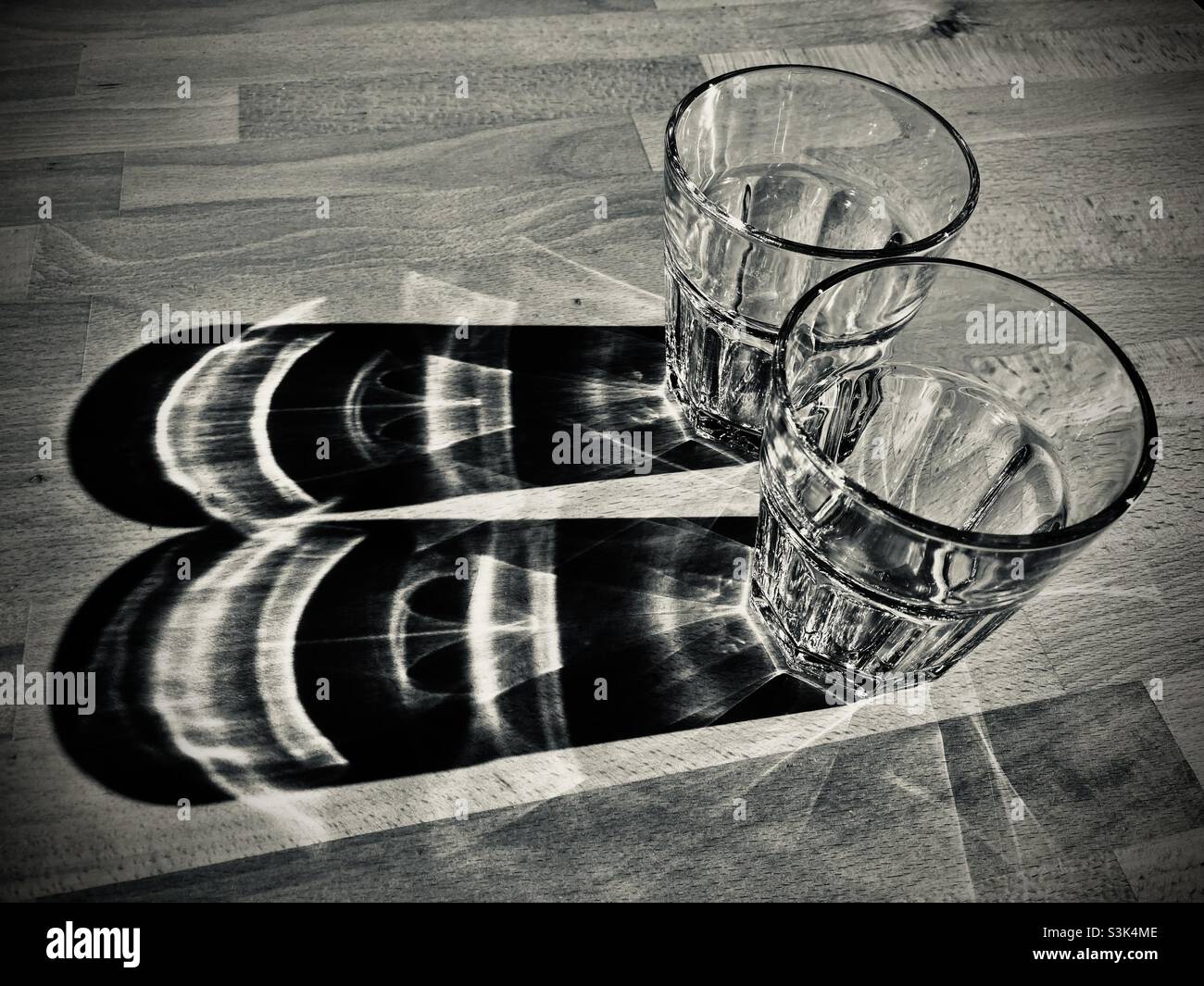 Deux verres d'eau se tenant sur une table en bois et jetant de longues ombres Banque D'Images