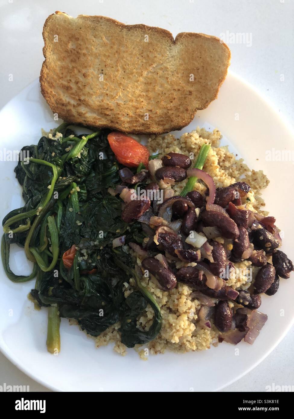 Le repas vegan se compose d'épinards de blé bulgur, de haricots rouges et d'oignons rouges et d'une tranche de pain Banque D'Images