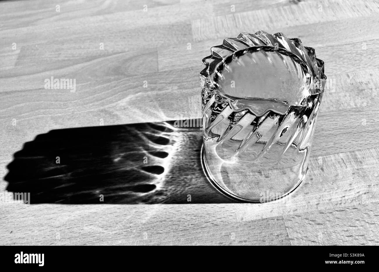 un verre d'eau se tient sur une table en bois et projette une ombre longue Banque D'Images