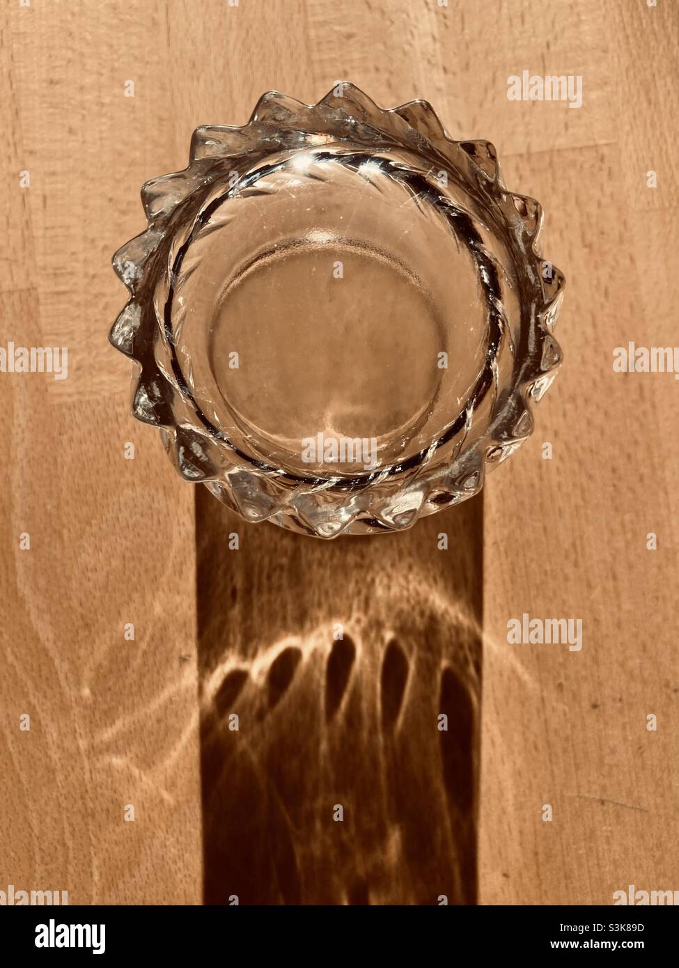 un verre d'eau se tient sur une table en bois et projette une ombre longue - Image de stock capturée avec un smartphone