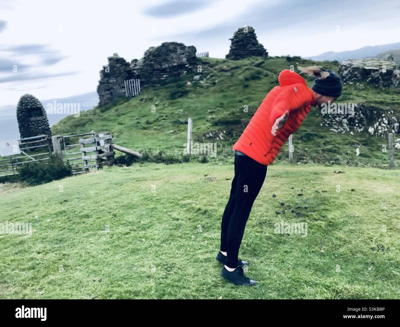 Une femme en blouson rouge se penche dans un vent fort près d'une ruine en Écosse au Royaume-Uni - Image de stock capturée avec un smartphone