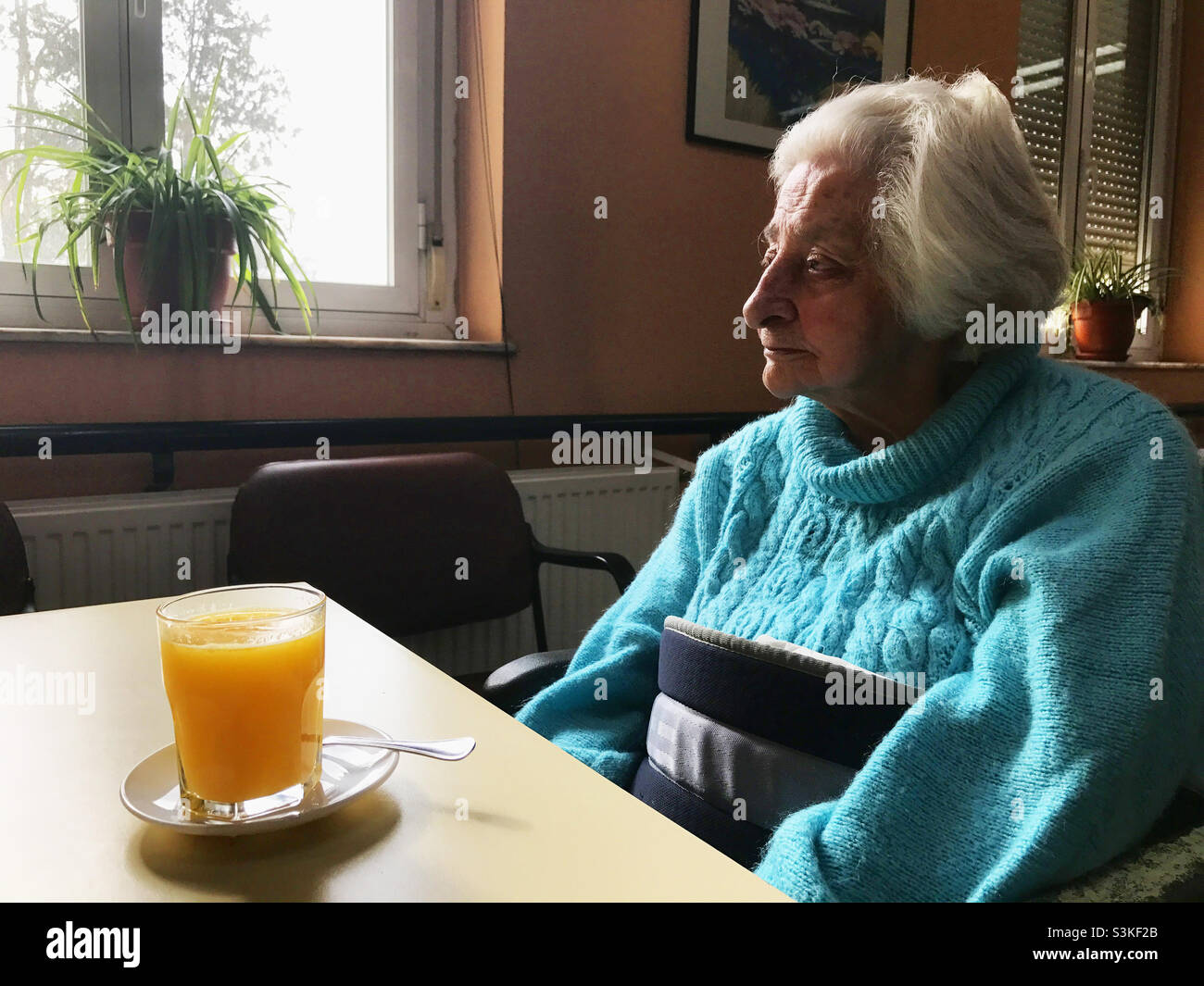 Femme âgée assise près d'une table avec du jus d'orange. - Image de stock capturée avec un smartphone