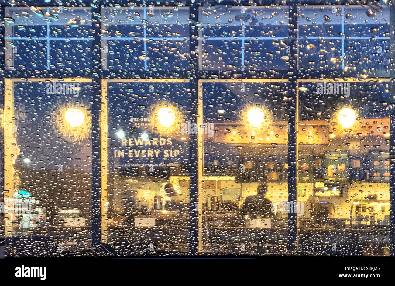 Regarder à travers un pare-brise couvert de gouttes de pluie dans la lueur chaude d'un café.Calgary, Alberta, Canada. Banque D'Images