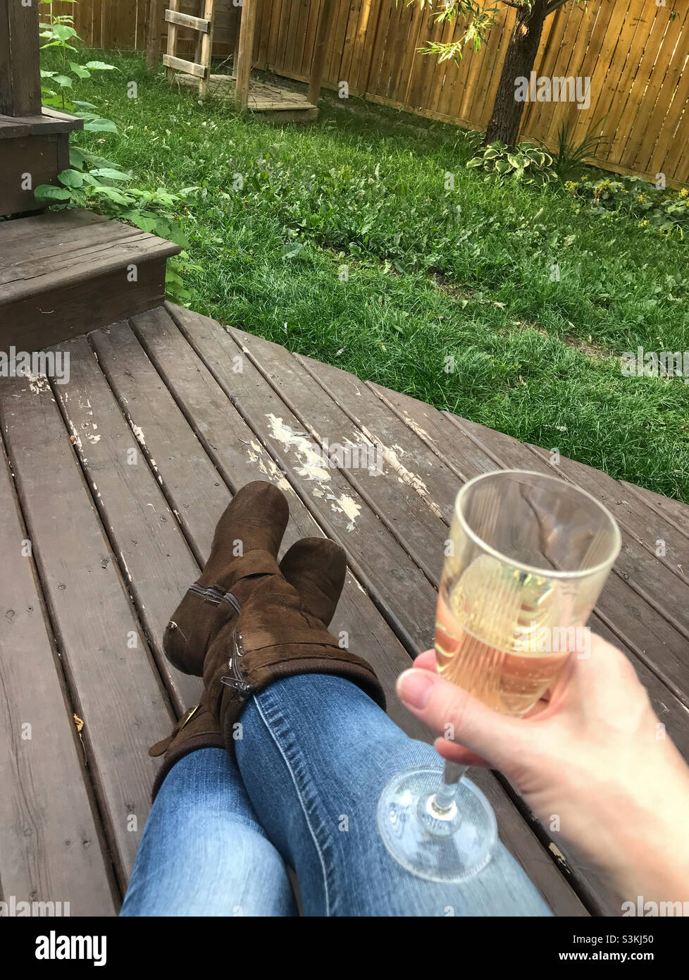 Une femme se détendant sur une terrasse, regardant les mauvaises herbes pousser, tout en appréciant un verre de bulles. Banque D'Images