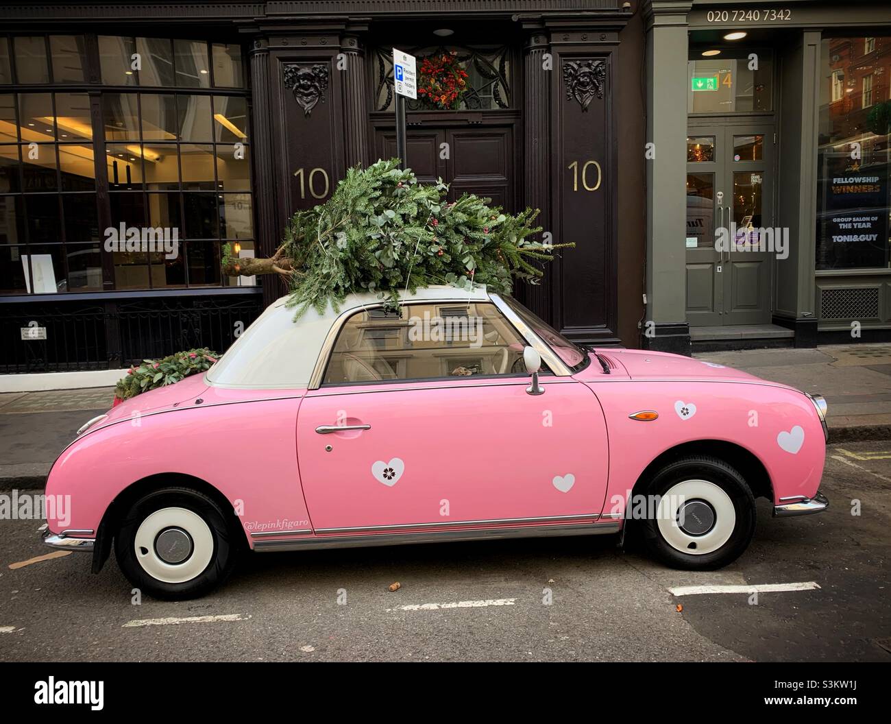 Une voiture rose est vue avec un arbre de Noël attaché au toit dans le centre de Londres. Banque D'Images