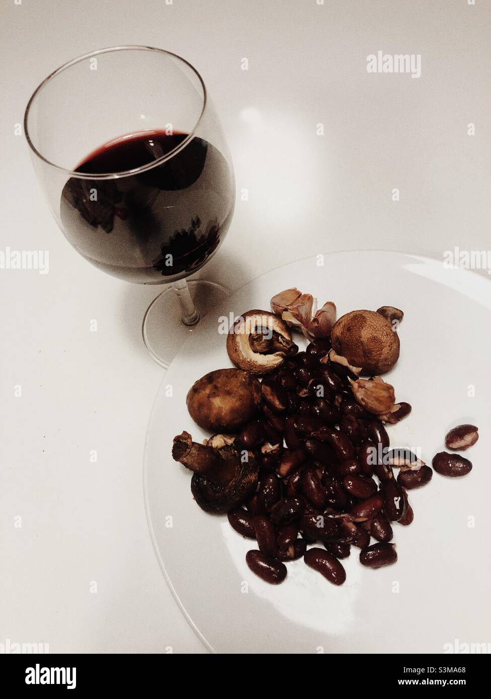 Un verre de vin rouge et quelques haricots rouges et champignons sont servis sur une assiette blanche sur fond blanc Banque D'Images