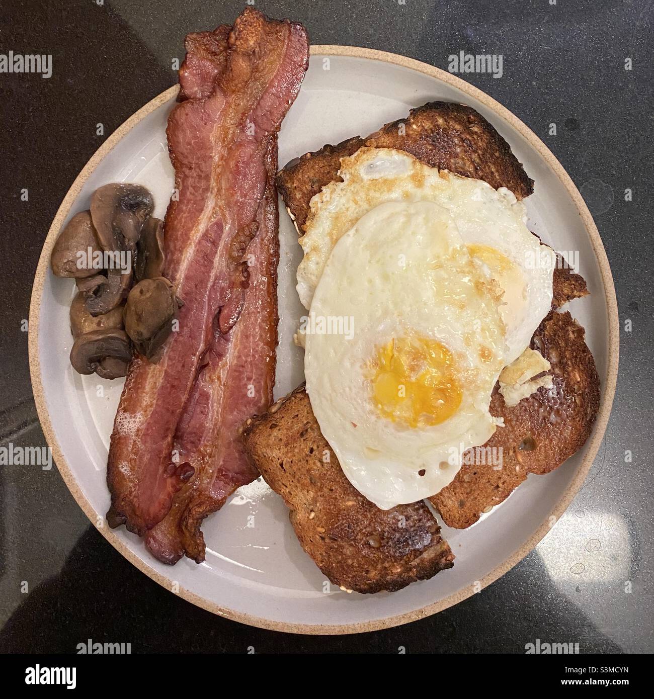 Assiette de petit déjeuner avec bacon frit, œufs sur Easy, toasts et champignons Banque D'Images