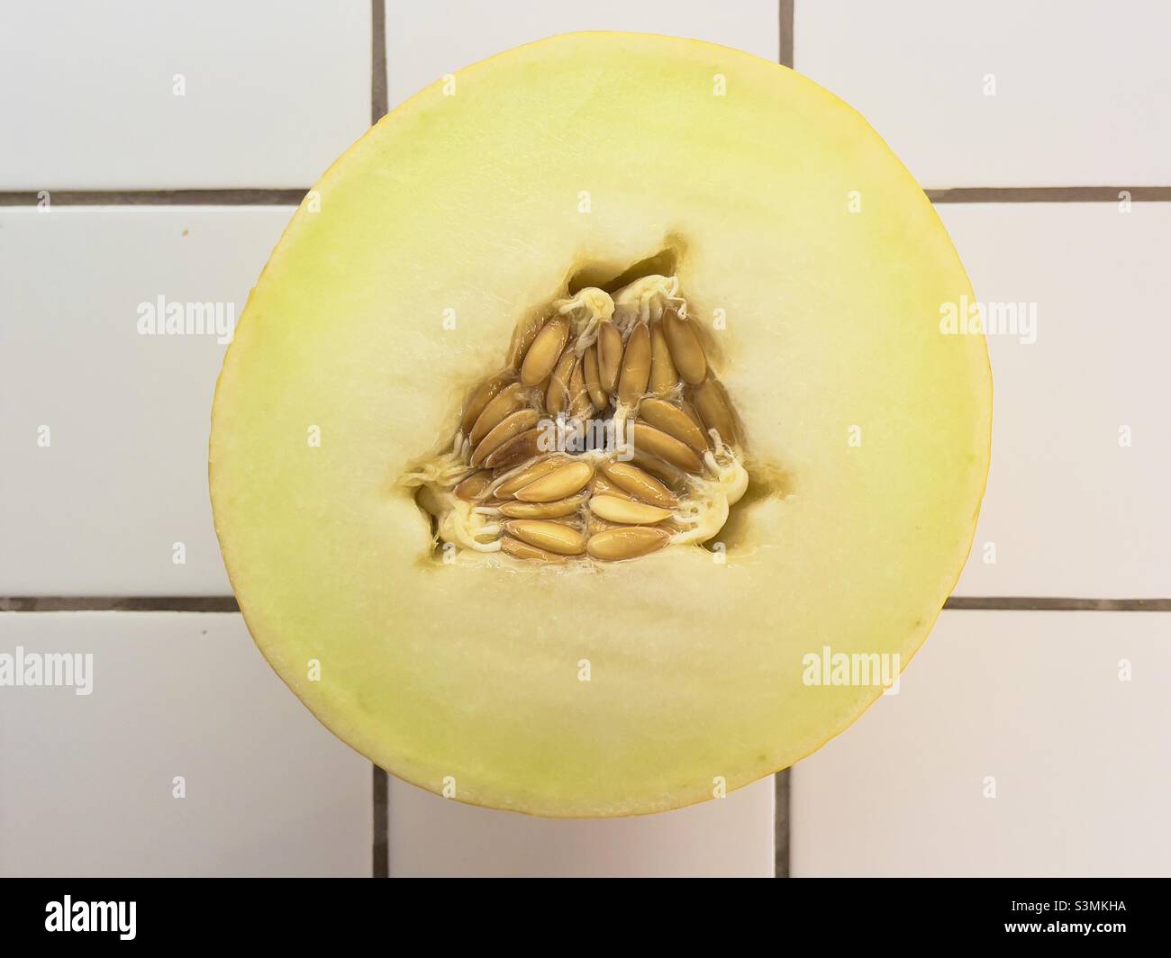 Un demi-melon canari montrant une coupe transversale avec les pépins ou les graines dans l'arrangement triangulaire caractéristique, reposant sur un plan de travail blanc carrelé Banque D'Images