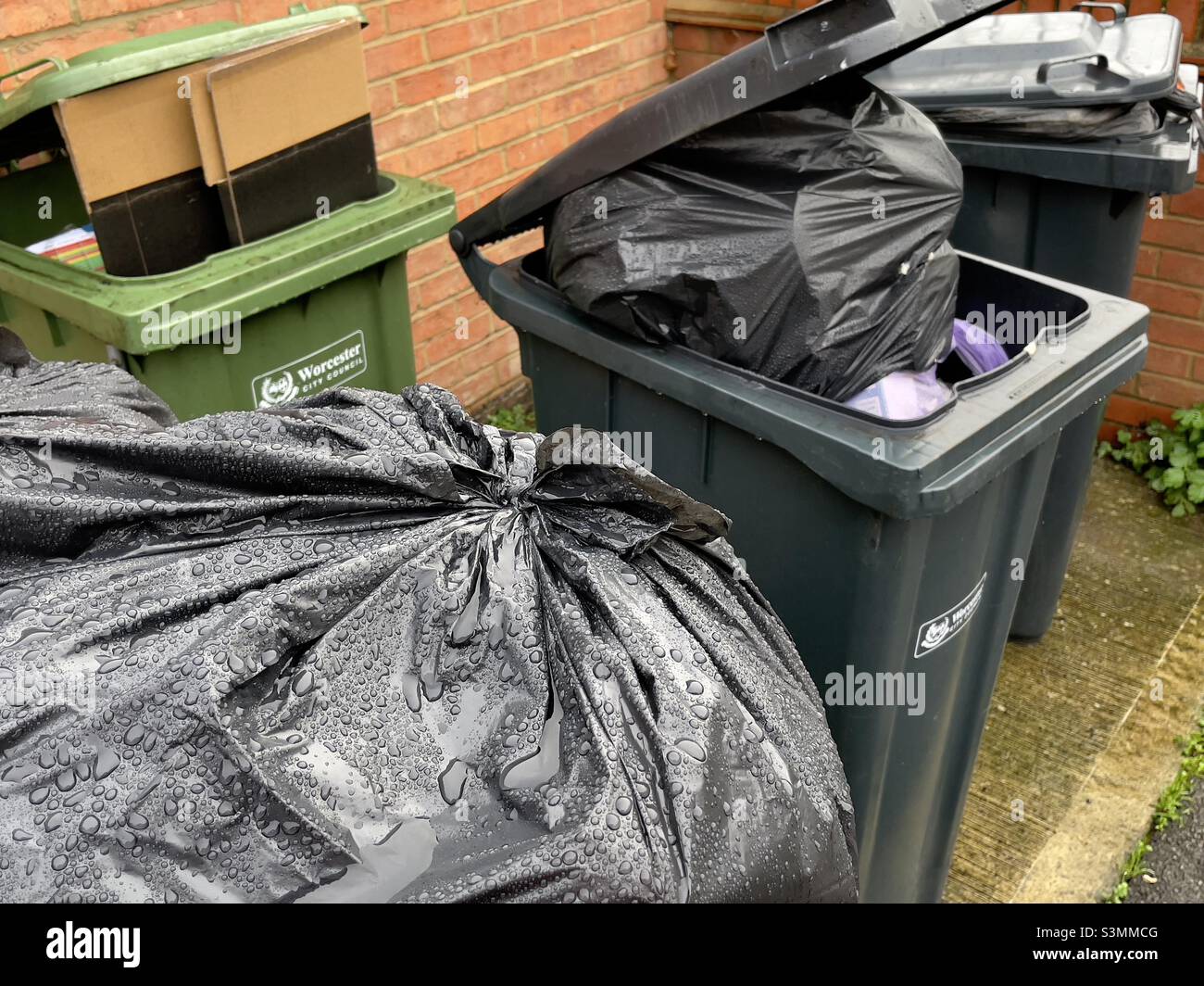 Une rangée de bennes à roulettes qui se sont enfouies de déchets en attente de collecte dans une rue de la banlieue de Worcester Banque D'Images
