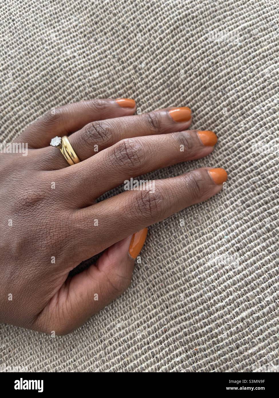 Main de peau brune avec ongles peints en orange sur un fond de jet texturé Banque D'Images