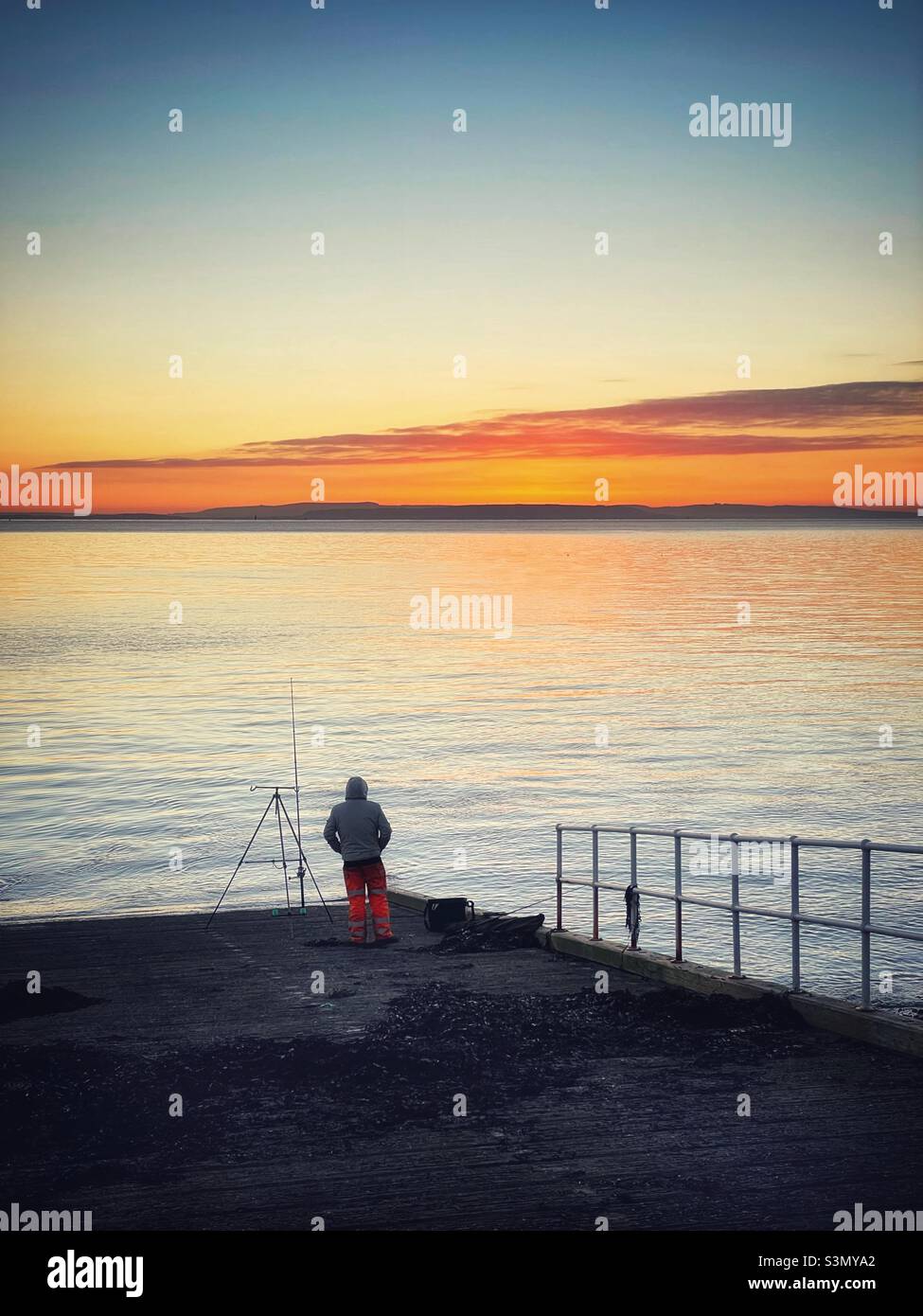 Pêcheur solitaire sur le front de mer de Penarth au lever du soleil, au sud du pays de Galles, janvier. Banque D'Images