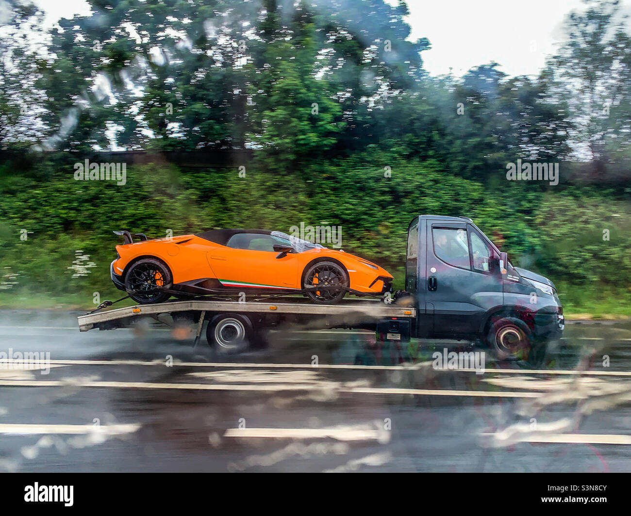 Lamborghini Huracan LP-640 Performante en orange à l'arrière d'un camion-remorque sur autoroute sous la pluie Banque D'Images