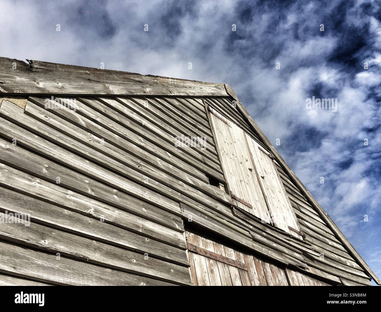 Vue abstraite d'un ancien bâtiment en bois à Thornham, Norfolk, Angleterre contre un ciel bleu et des nuages blancs. - Image de stock capturée avec un smartphone