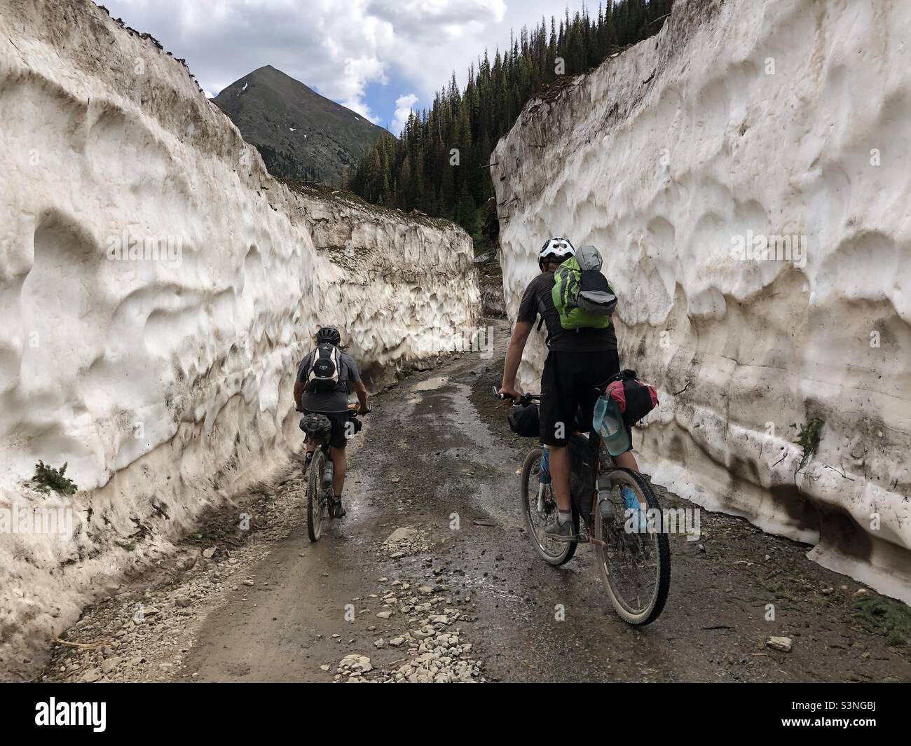 Deux hommes en vélo se dressent entre les imposants murs de neige du Colorado après une avalanche. Banque D'Images