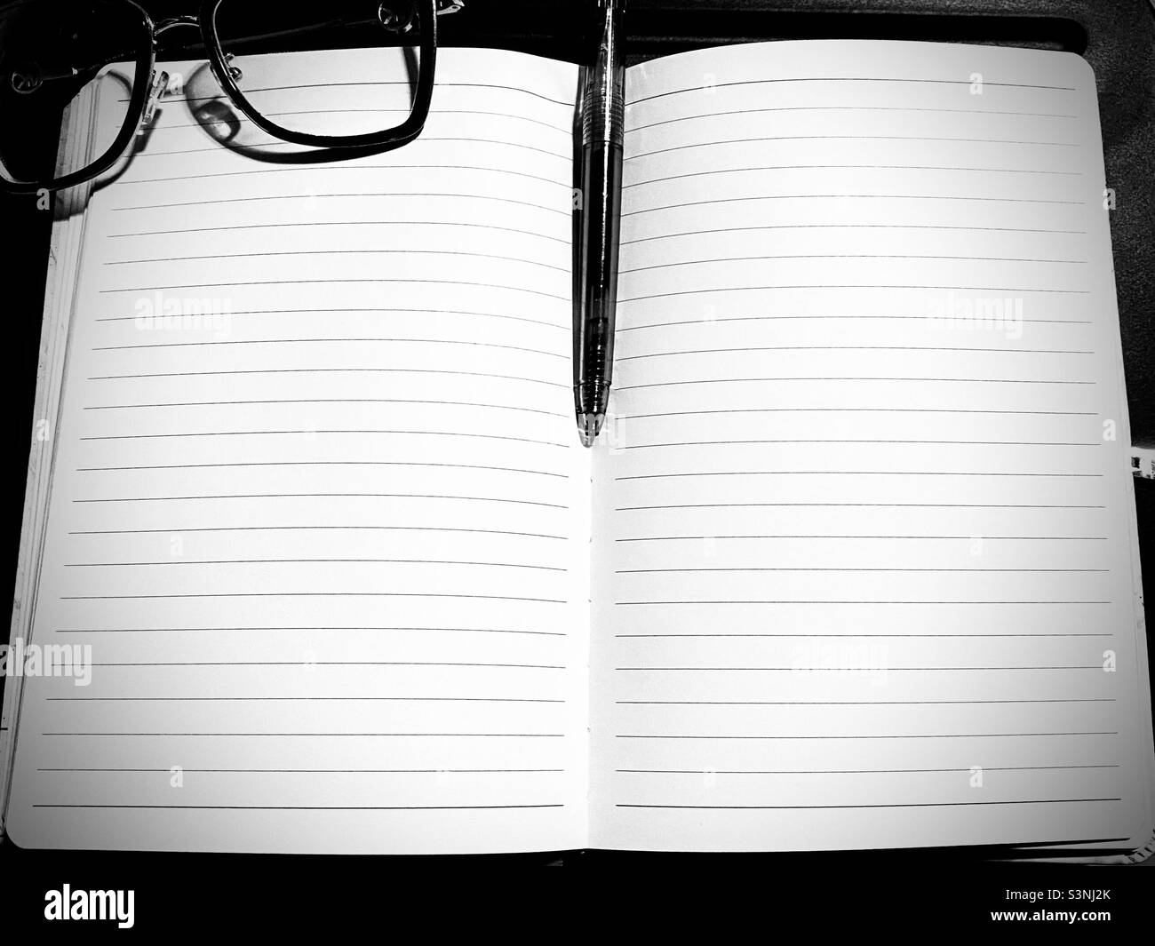 Pose à plat en noir et blanc avec un carnet ouvert, des pages vierges, un stylo à encre et des lunettes sur un bureau pour ordinateur portable, du papier vierge ; Livre ouvert, journal Banque D'Images