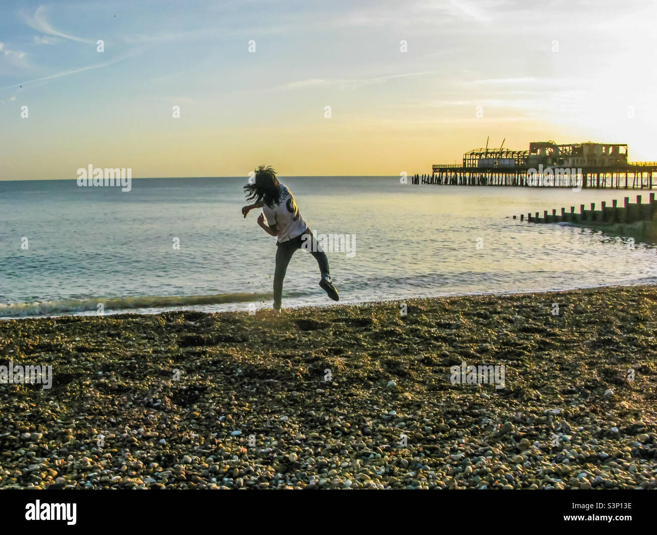 Au cours d'un après-midi chaud de façon insaison en janvier 2012, un jeune homme s'embarque pour jeter des pierres dans la mer à la plage de Hastings, à côté des restes brûlés de la jetée - Image de stock capturée avec un smartphone