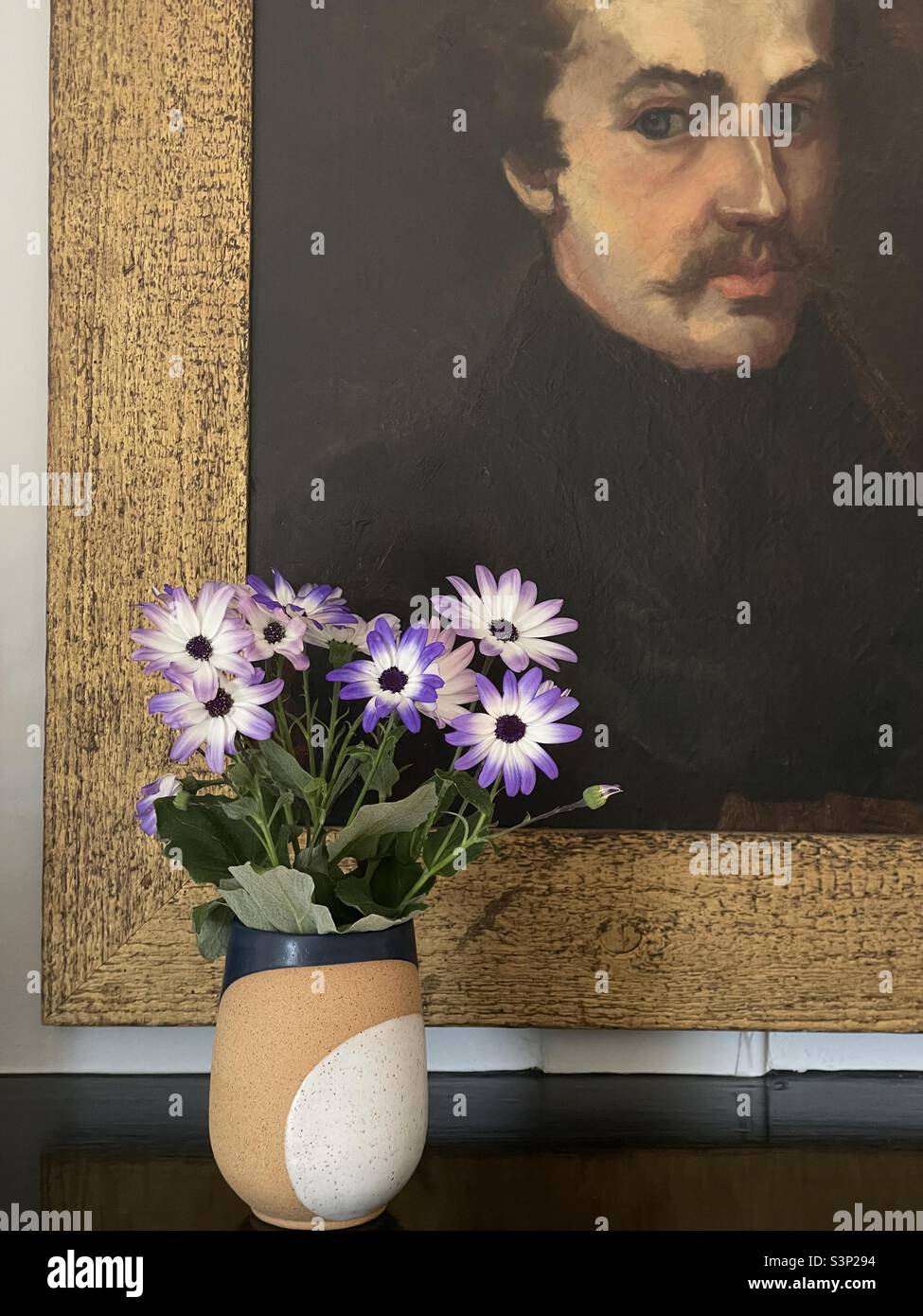 Fleurs violettes et blanches dans un vase au-dessous d'un portrait peint Banque D'Images