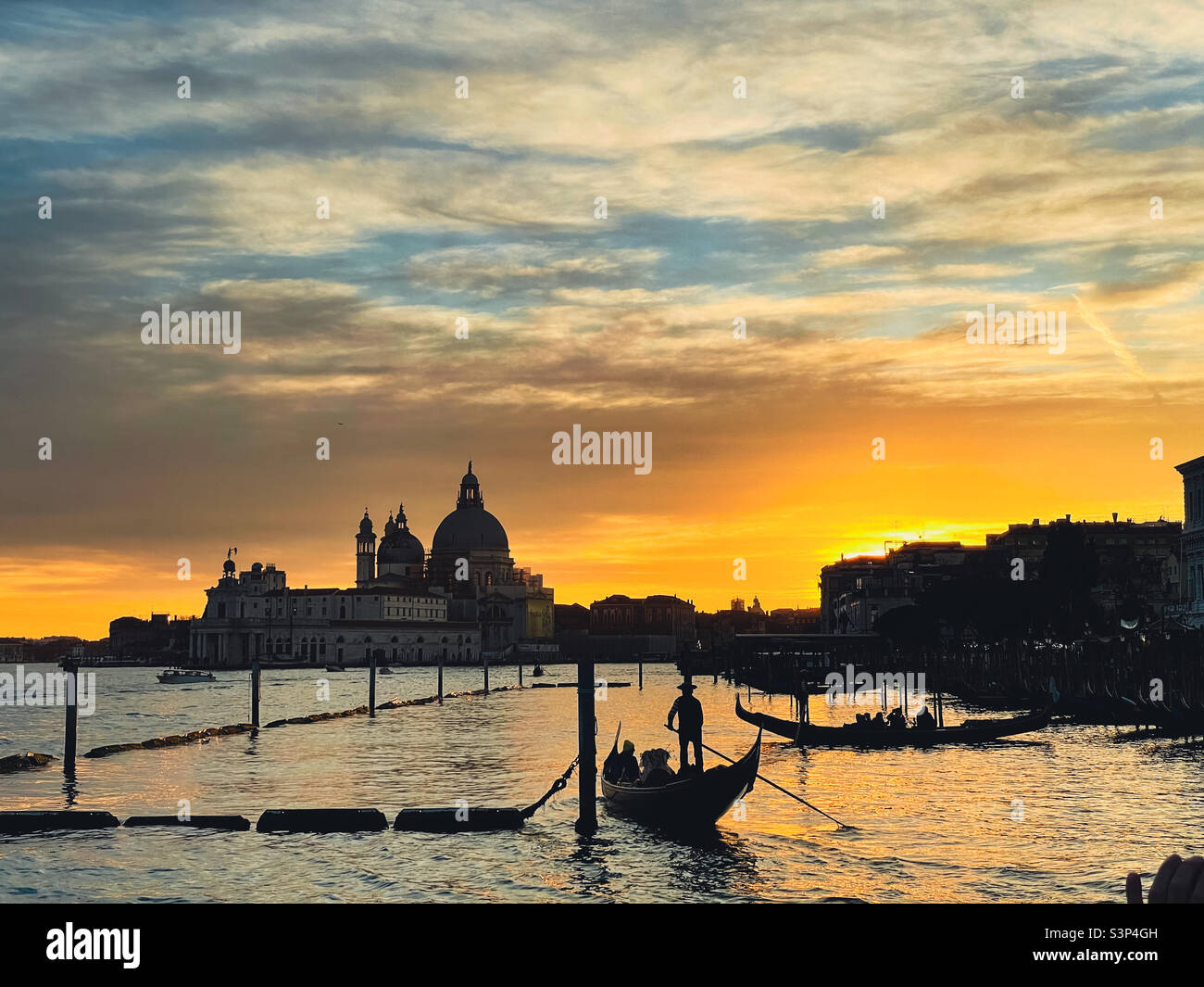 Silhouette d'un gondolier au coucher du soleil avec toile de fond des monuments vénitiens. Banque D'Images