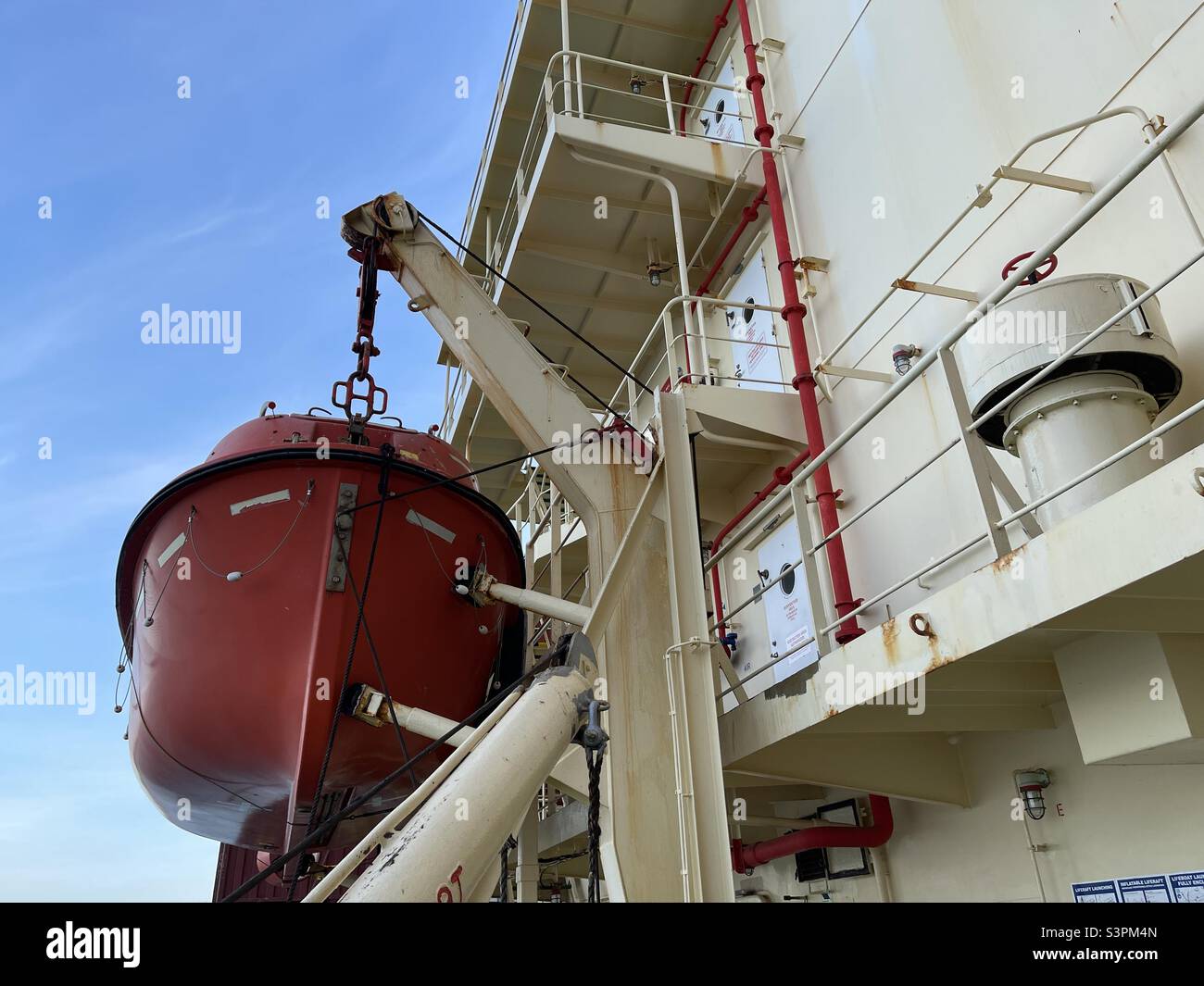 Orange Lifeboat sécurisé sur davit de. Côté tribord du récipient près de la superstructure peinte de couleur crème. La vue est depuis la plate-forme d'embarquement du bateau pendant la journée ensoleillée et le printemps temps calme. Banque D'Images