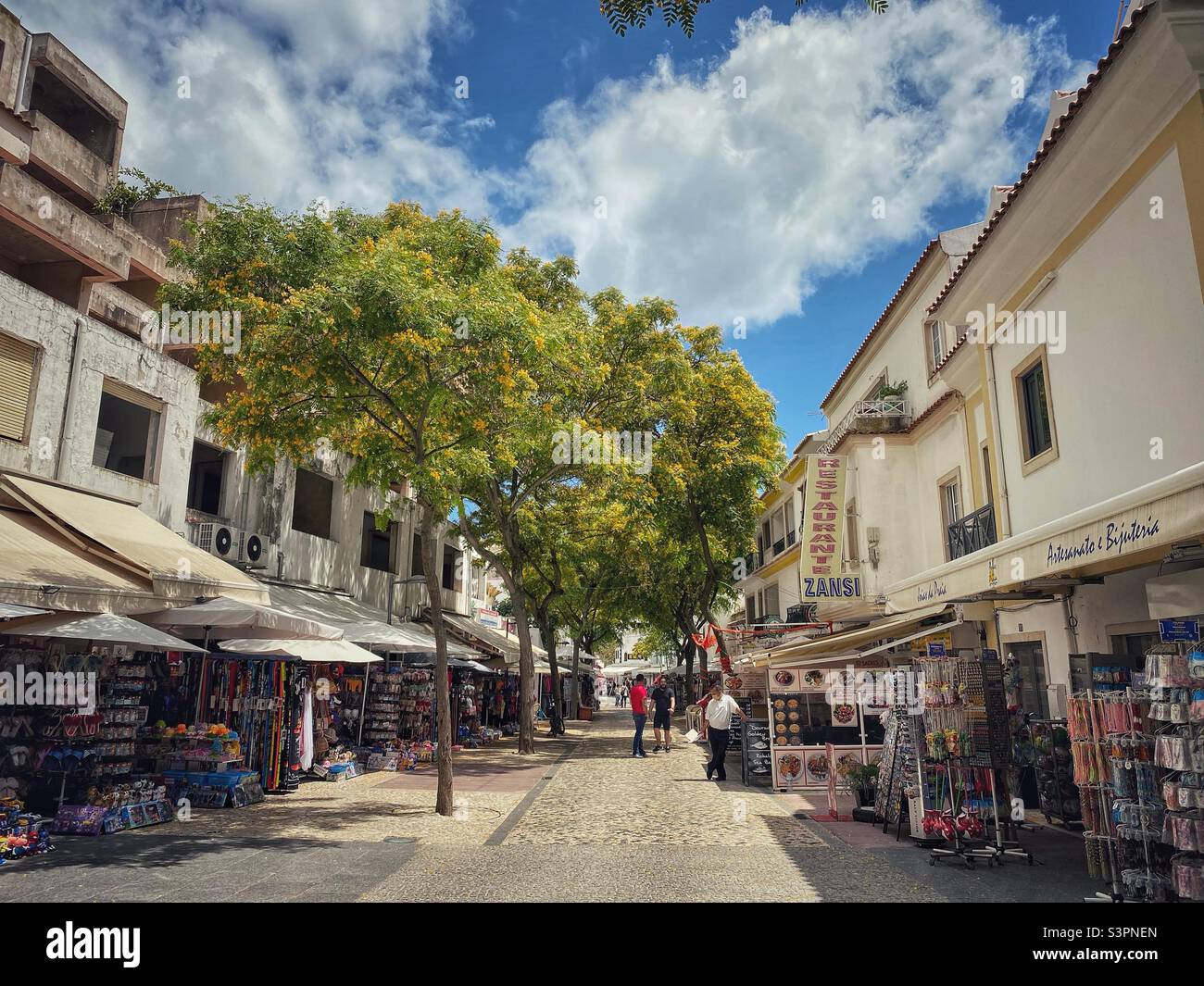 Rue commerçante piétonne traditionnelle avec arbres fleuris à Albufeira, Algarve, Portugal. Banque D'Images