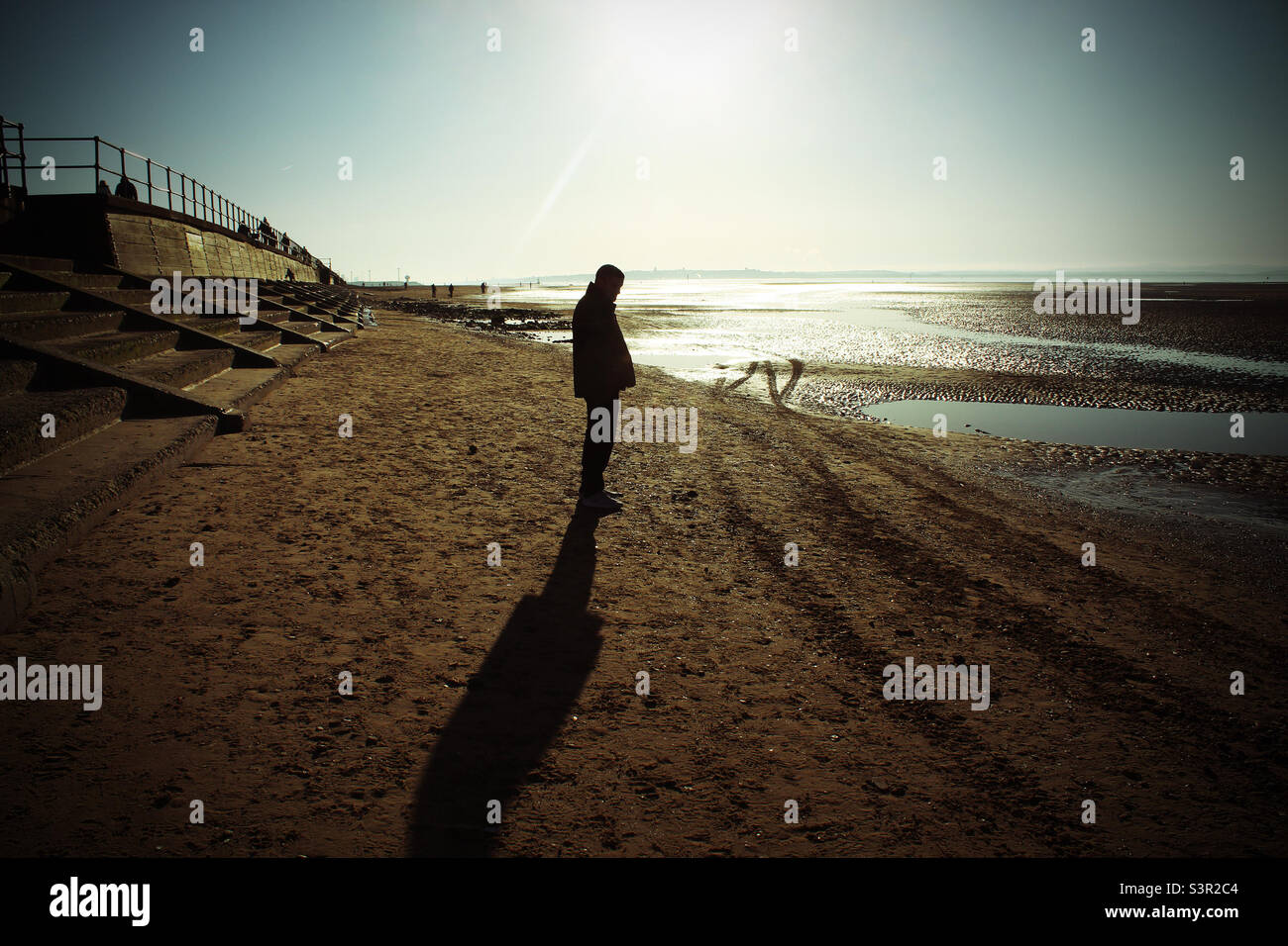 Jeune homme debout sur une plage et donnant sur la mer. La photo a été prise à la plage de Crosby à Liverpool, Merseyside - Image de stock capturée avec un smartphone