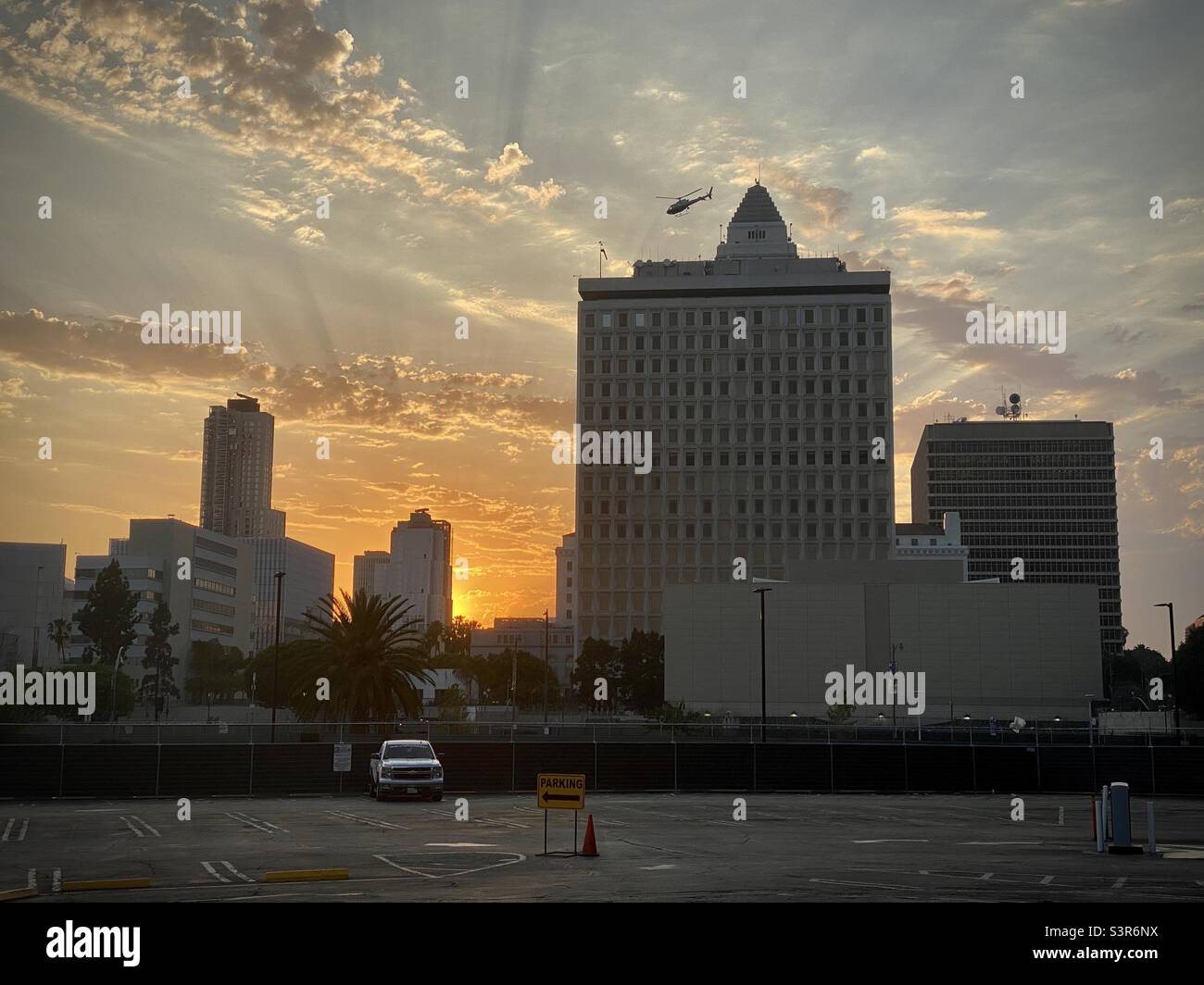 LOS ANGELES, CA, JUIN 2021 : un hélicoptère de police survole les bâtiments de la ville dans le centre civique du centre-ville avec le ciel de coucher de soleil en arrière-plan, parking en premier plan - Image de stock capturée avec un smartphone