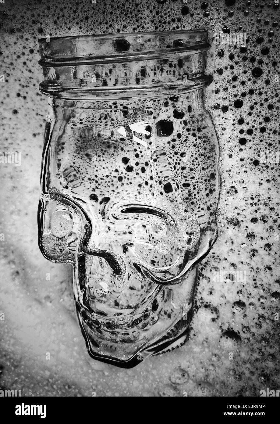 Une photographie en noir et blanc d'un pot en verre en forme de crâne dans un bol d'eau savonneuse Banque D'Images