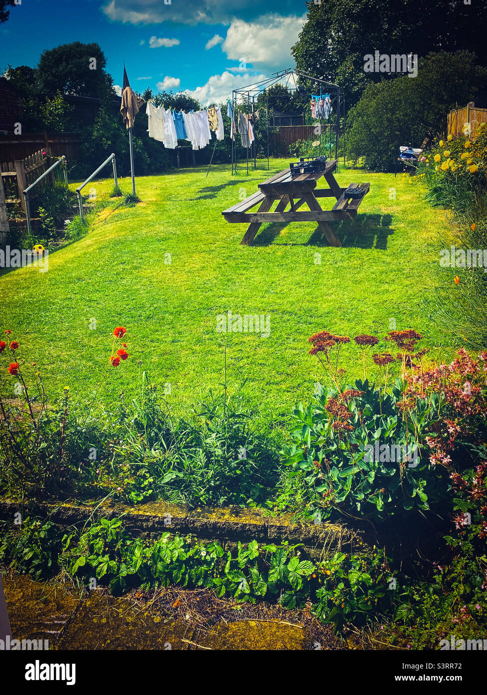 Une vue le long d'un jardin résidentiel avec une table de pique-nique et un sèche linge sur une ligne de lavage. Banque D'Images