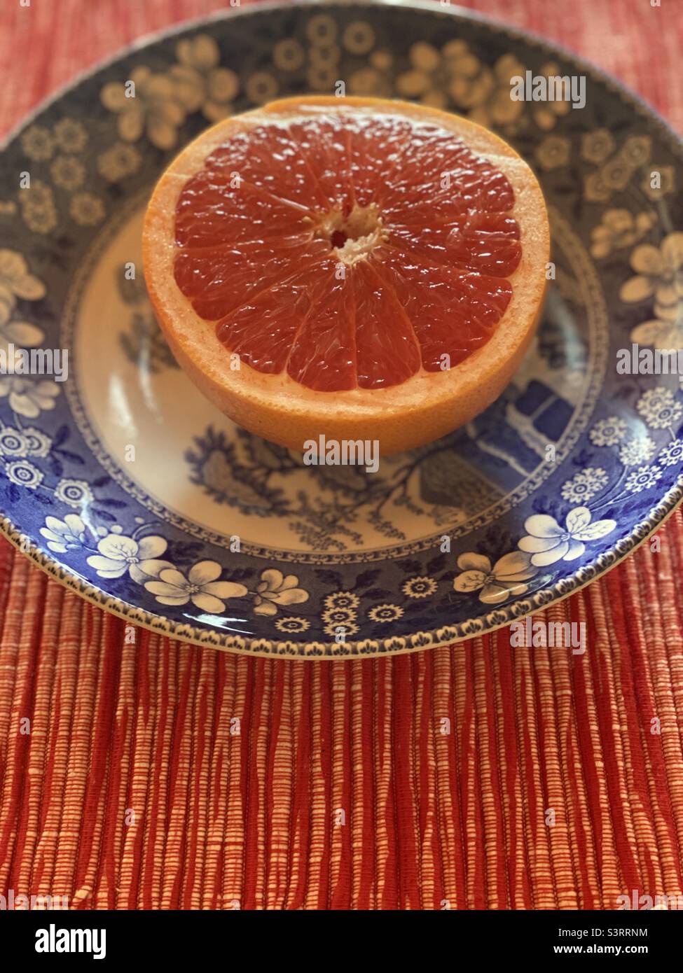 Un pamplemousse rouge juteux à moitié rubis sur une assiette pour le petit déjeuner Banque D'Images