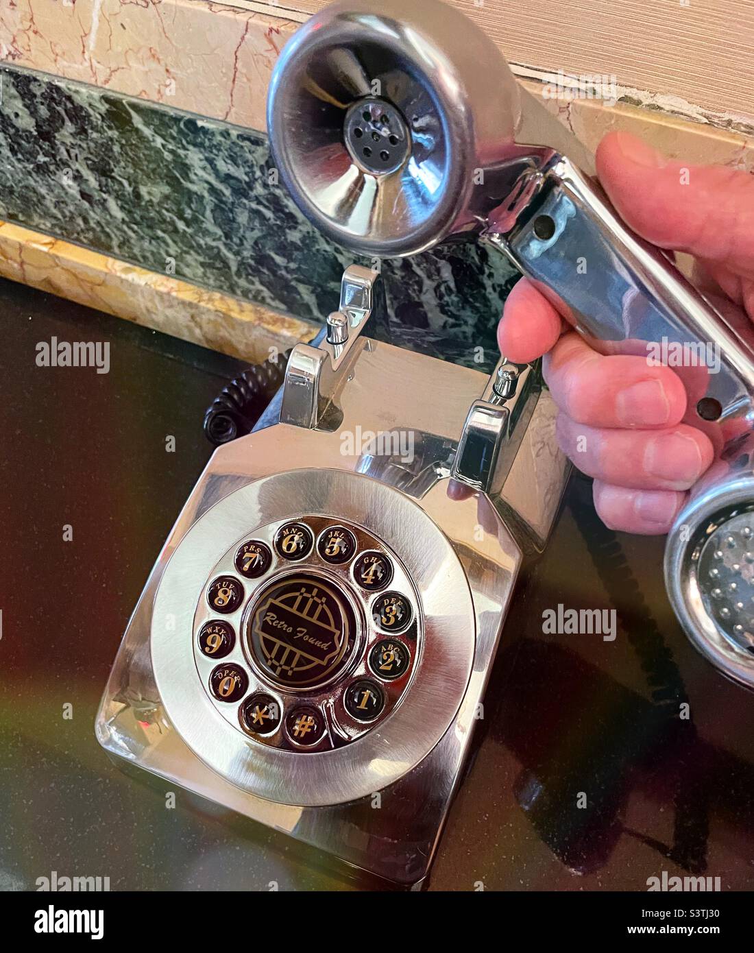 Un homme tenant le récepteur d'un téléphone à bouton-poussoir en argent métallique dans le hall de l'hôtel Edison de Times Square pour mettre à jour sa réservation, 2022, New York City, Etats-Unis - Image de stock capturée avec un smartphone