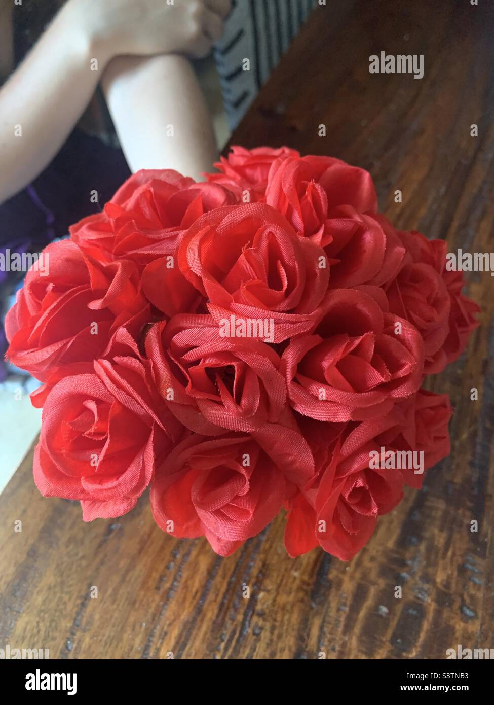 Bras de jeune femme tenant un bouquet de roses rouges sur une table en bois - Image de stock capturée avec un smartphone
